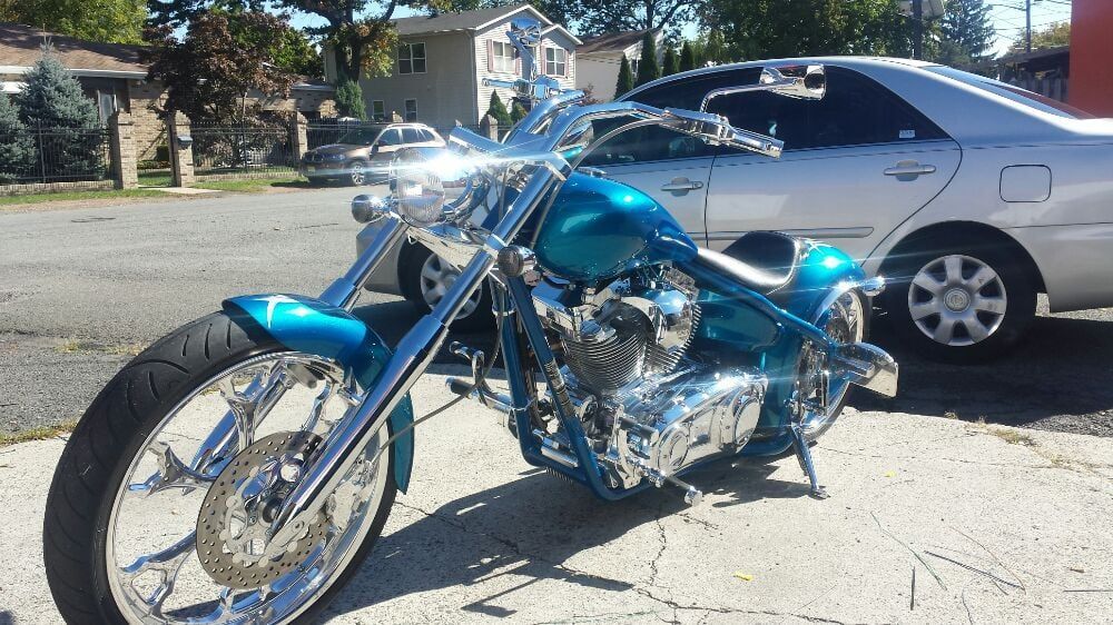 A blue motorcycle is parked on the side of the road next to a silver car.