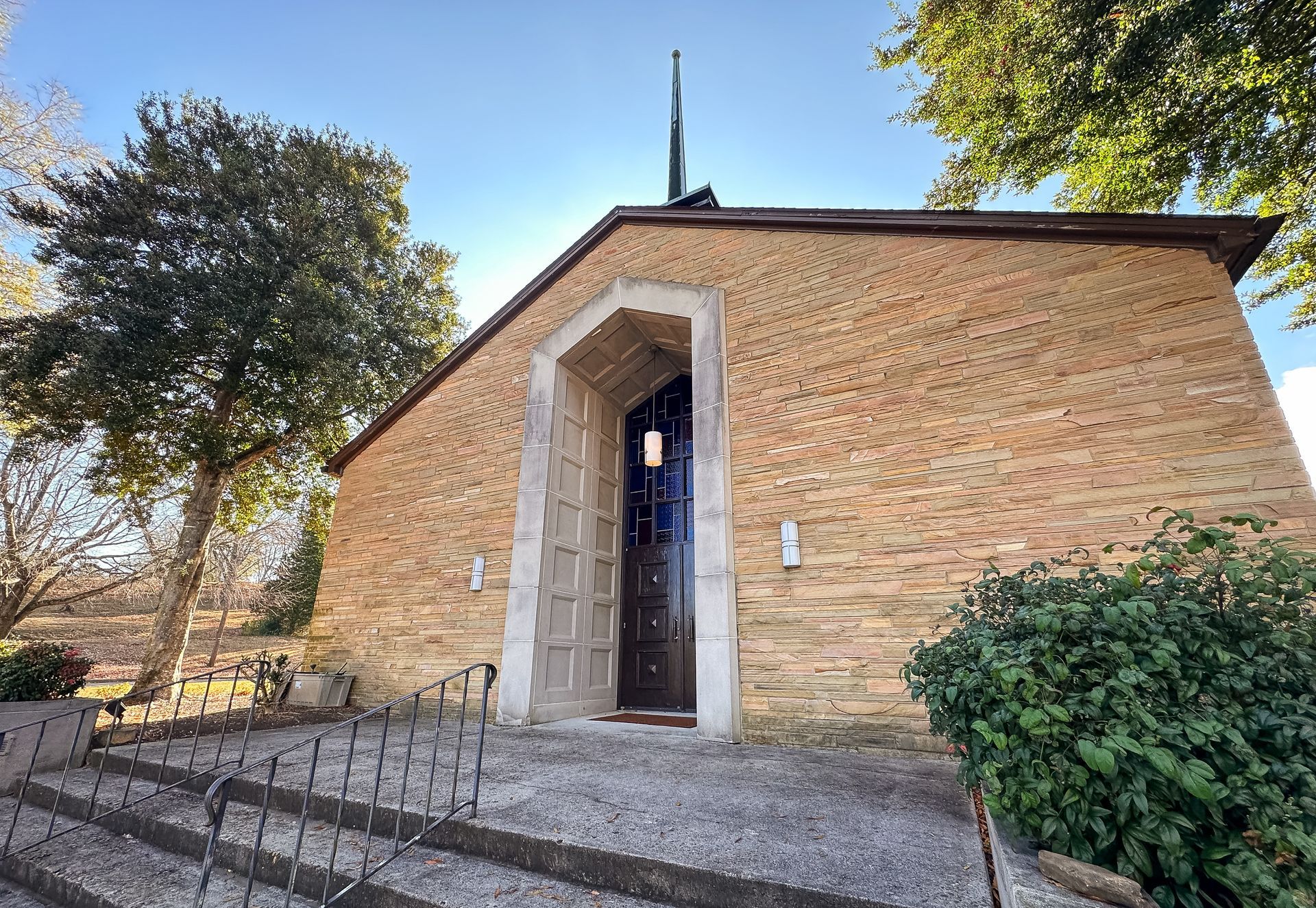 Stone chapel with a tall arched entryway, steps leading up to the entrance, and trees surrounding the building.