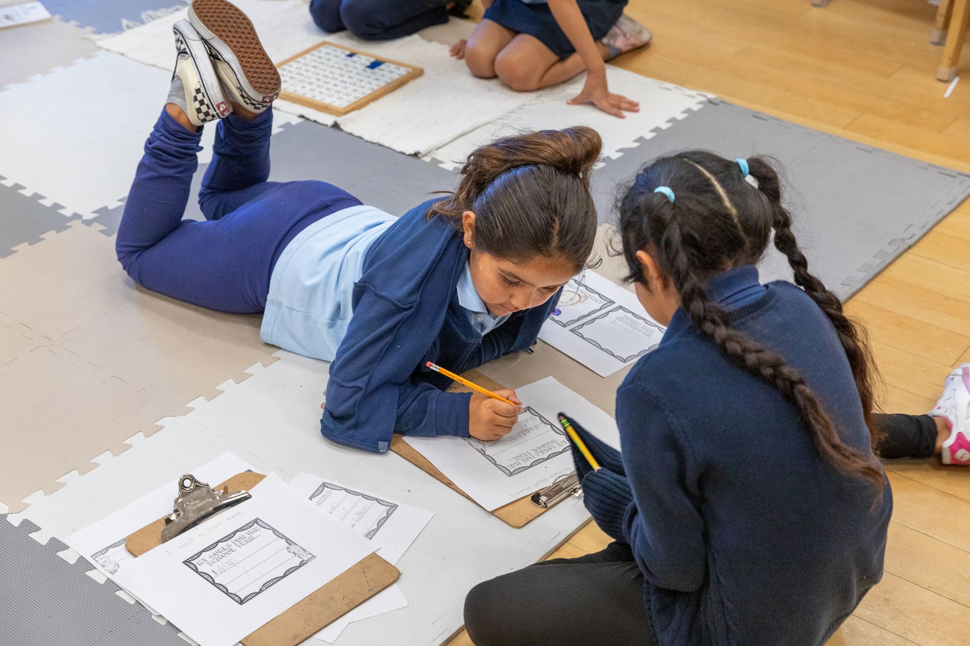 Two girls are laying on the floor writing on a clipboard