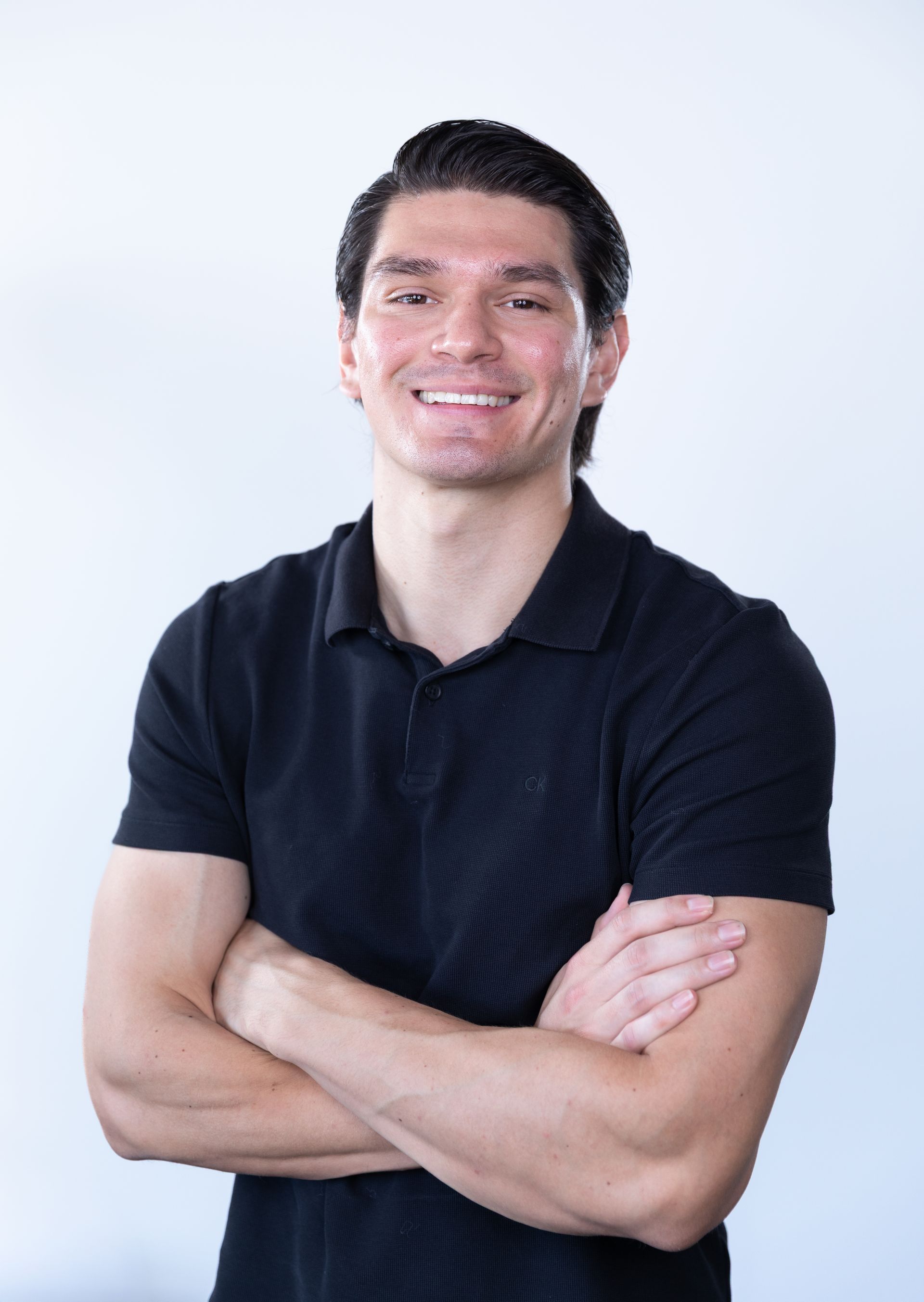 Smiling man in a black polo shirt with arms crossed against a light background