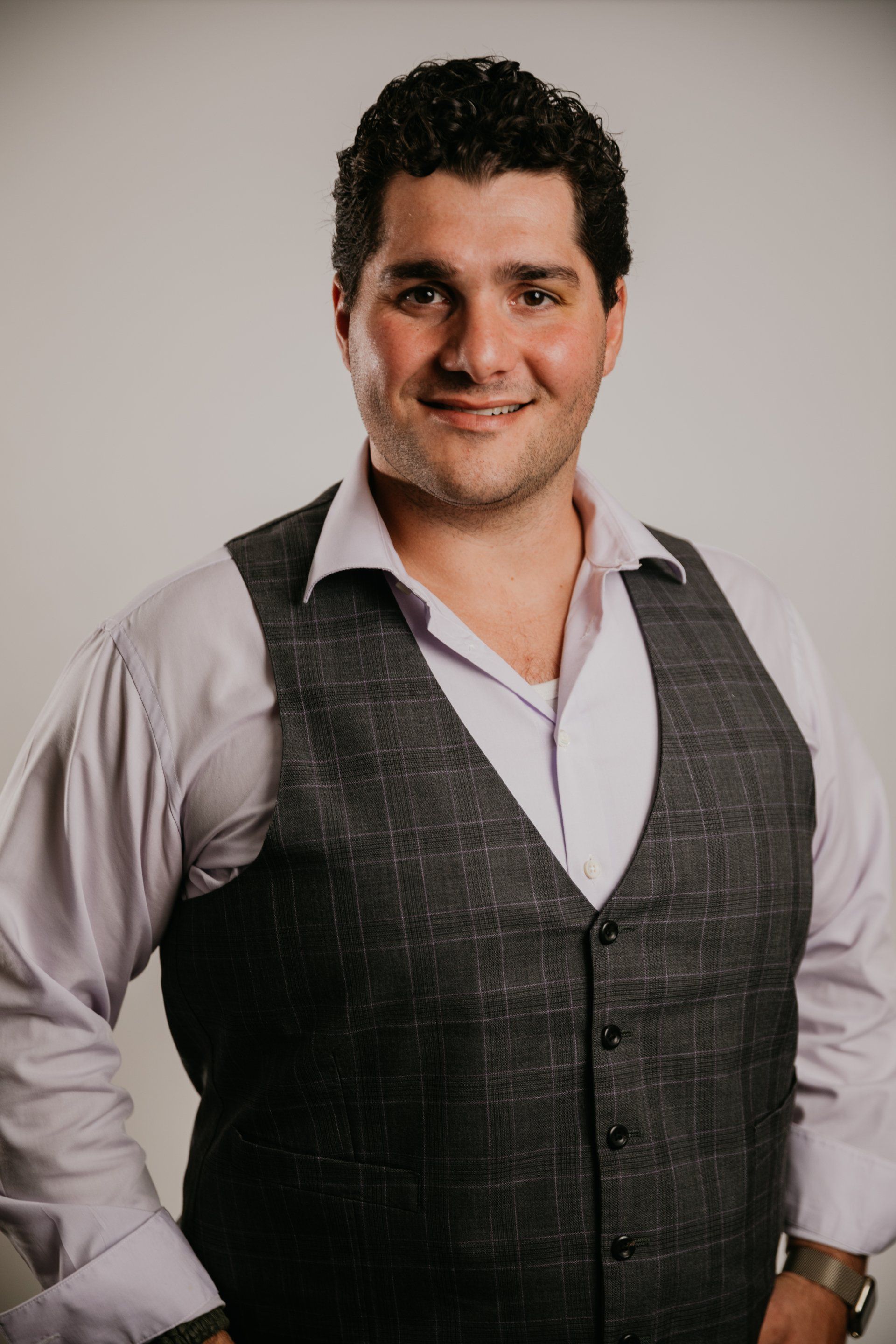 A man wearing a vest and a white shirt is smiling for the camera.