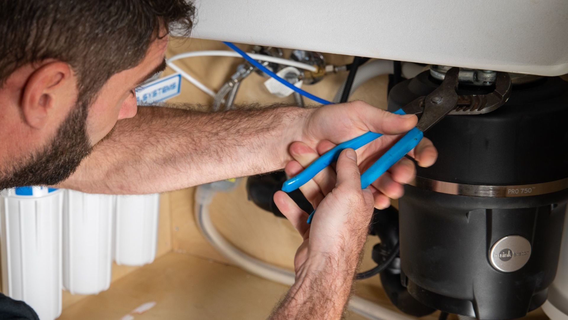 A man is fixing a garbage disposal with pliers