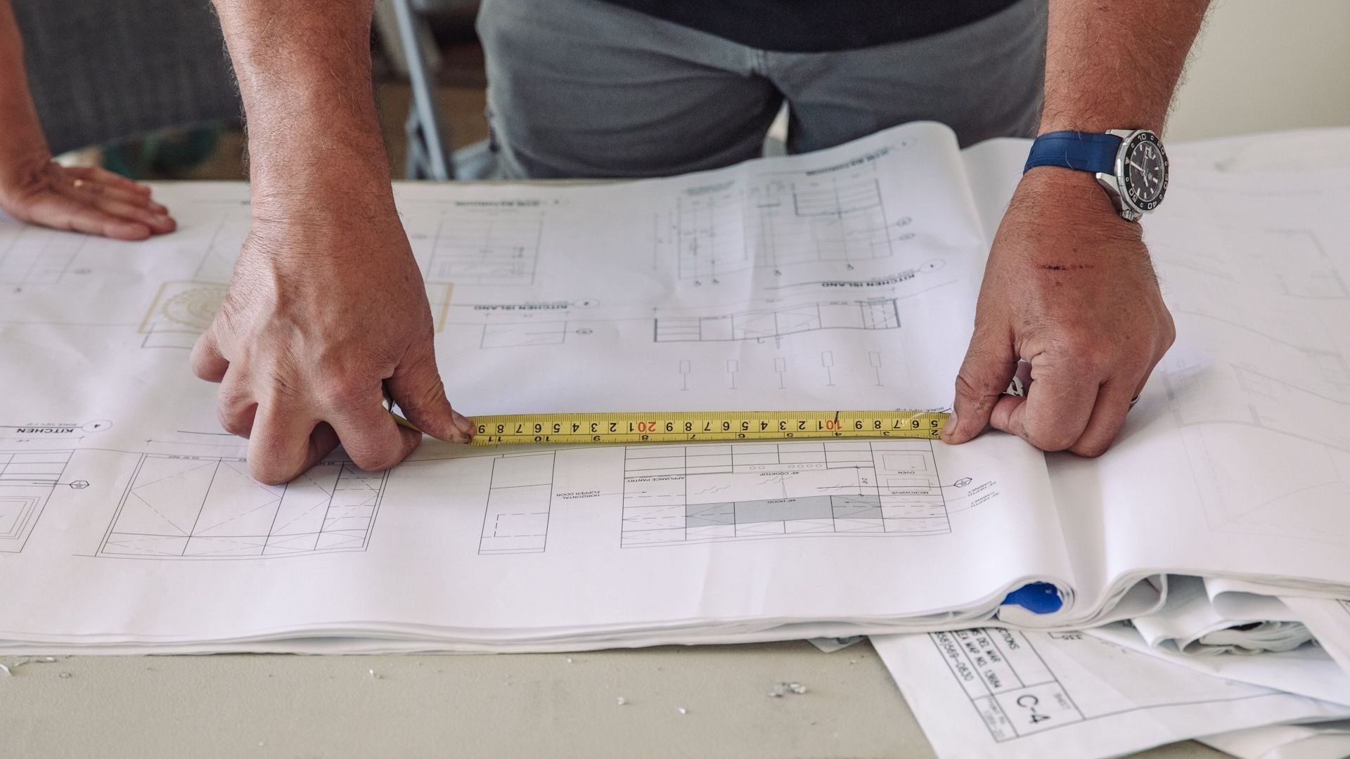 A man is measuring a blueprint with a tape measure