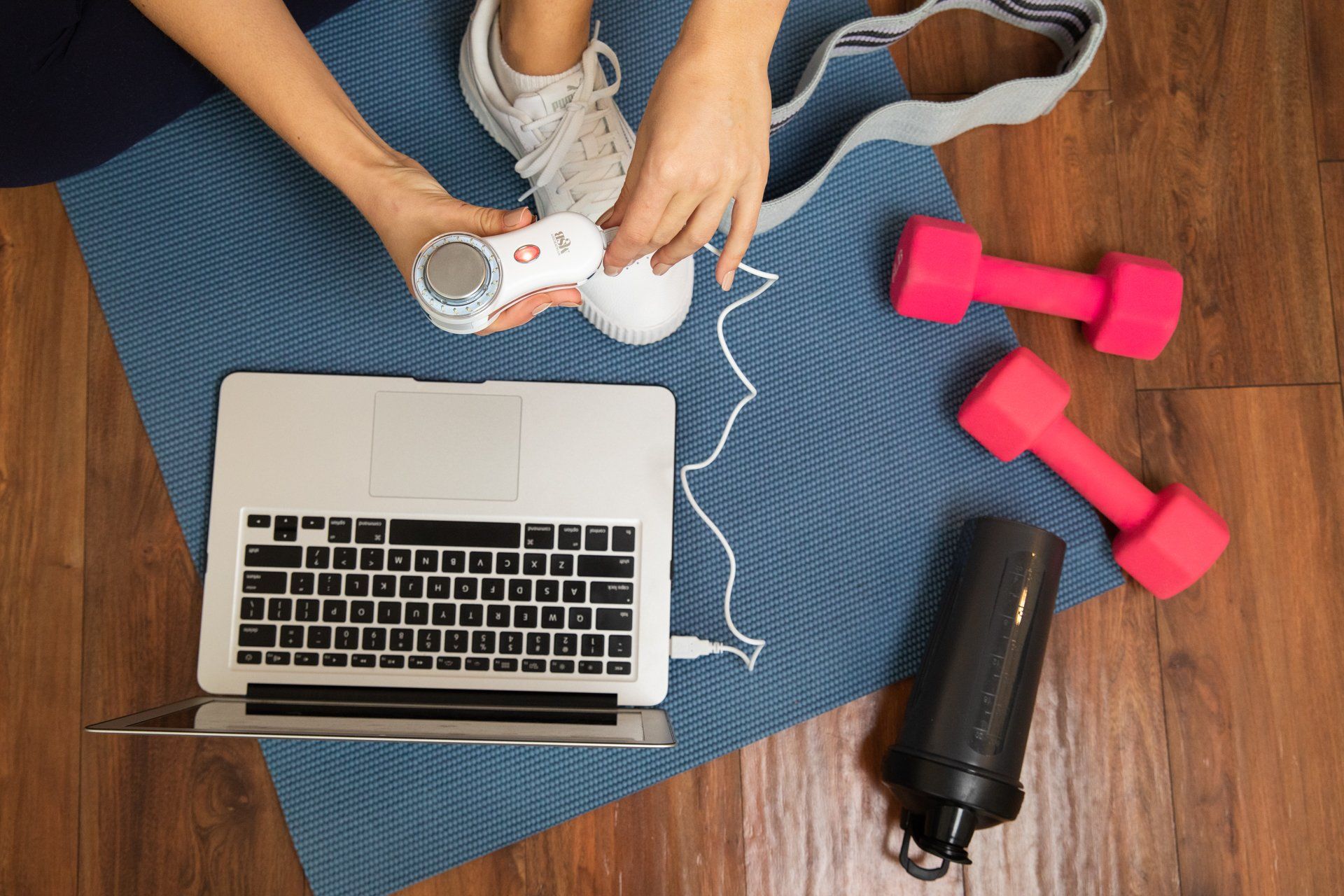 A person is tying their shoe next to a laptop and dumbbells