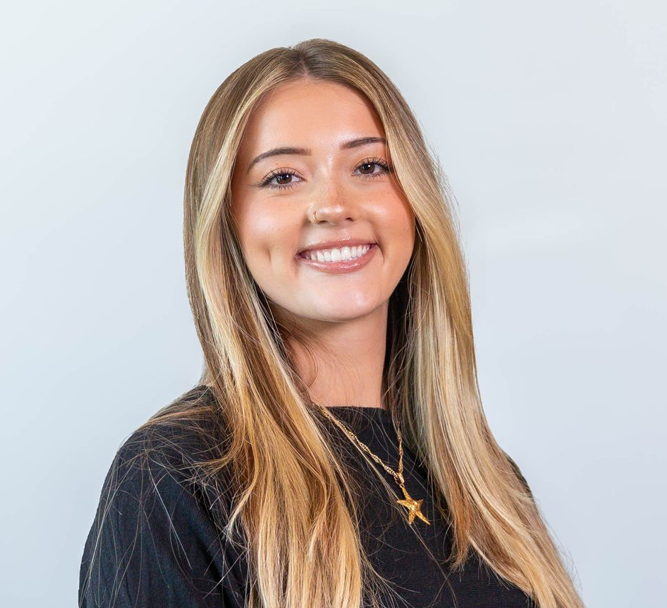 Smiling woman with long blonde hair wearing a black top against a light background