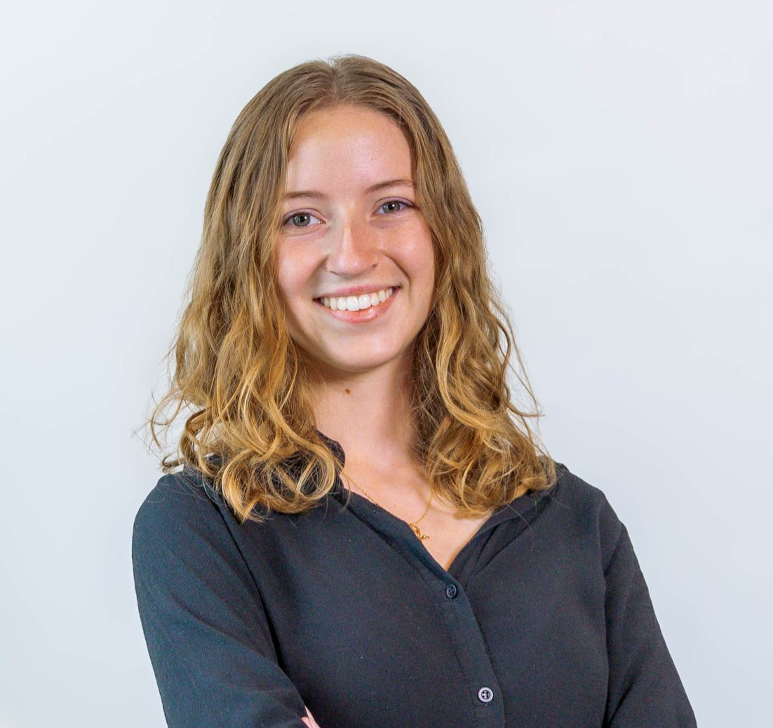 Smiling woman with curly blonde hair in a dark shirt against a light gray background
