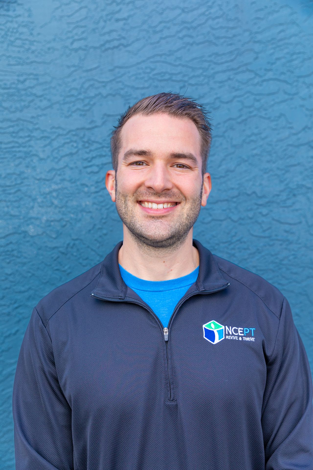A man wearing a blue shirt and a blue jacket is smiling for the camera