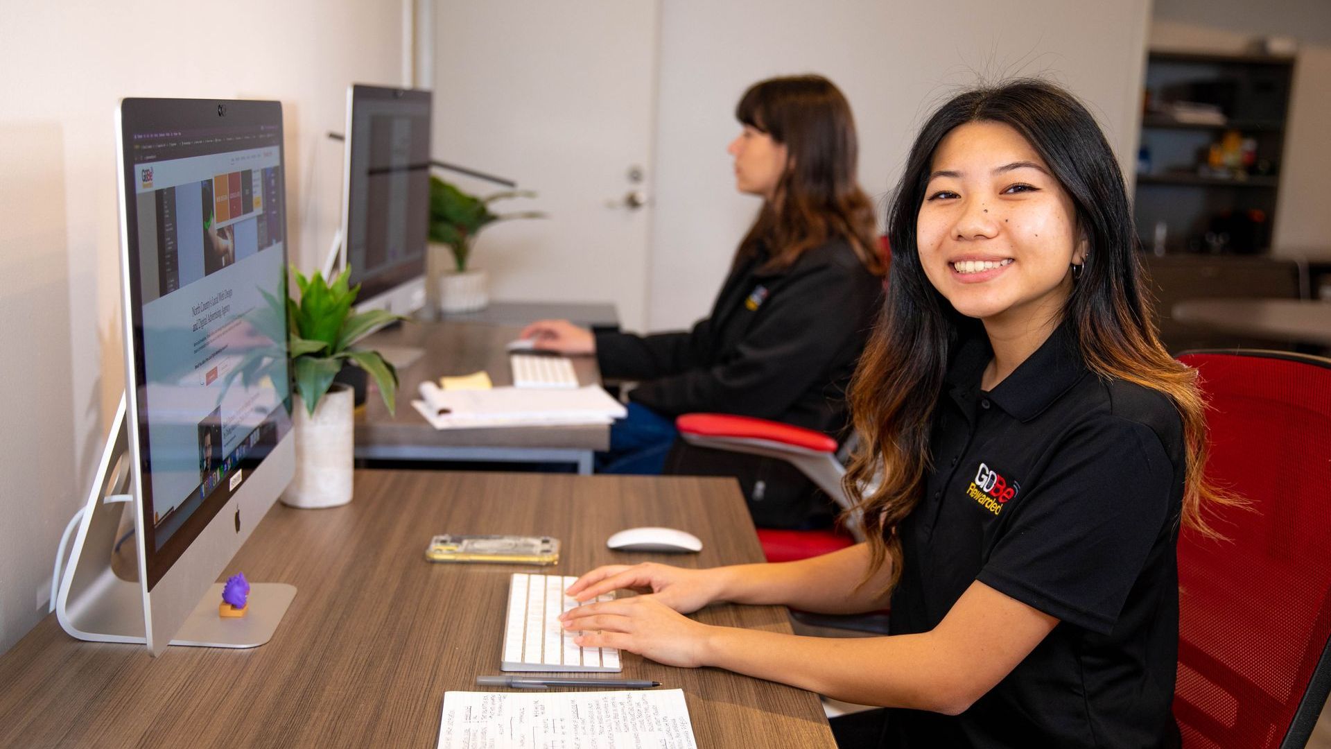 A woman in a black shirt is sitting at a desk in front of a computer.