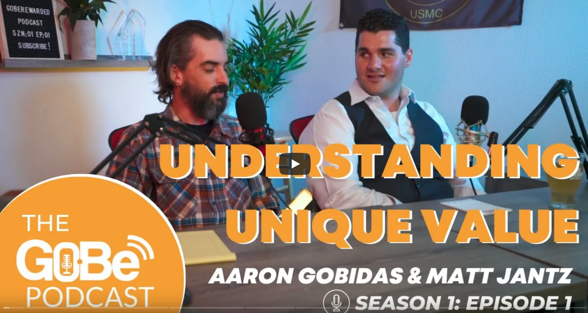Two men are sitting at a table with microphones and the words understanding unique value above them