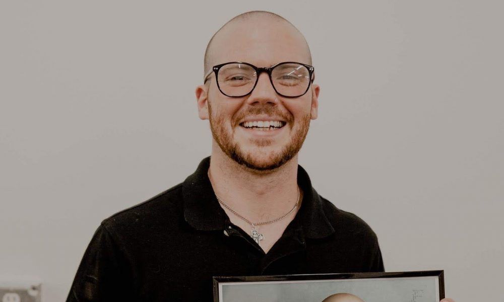 A man wearing glasses and a black shirt is holding a picture frame.
