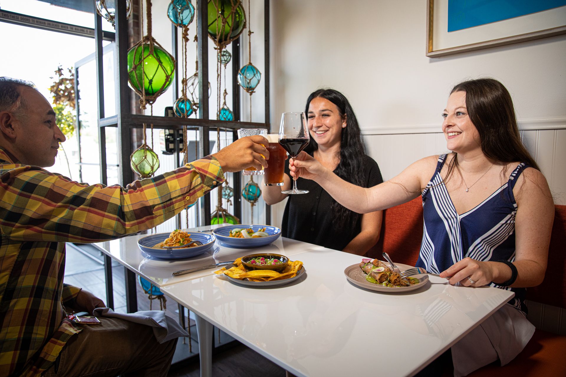 A man and two women are sitting at a table toasting with wine glasses