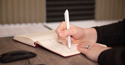 A person is writing in a notebook with a pen