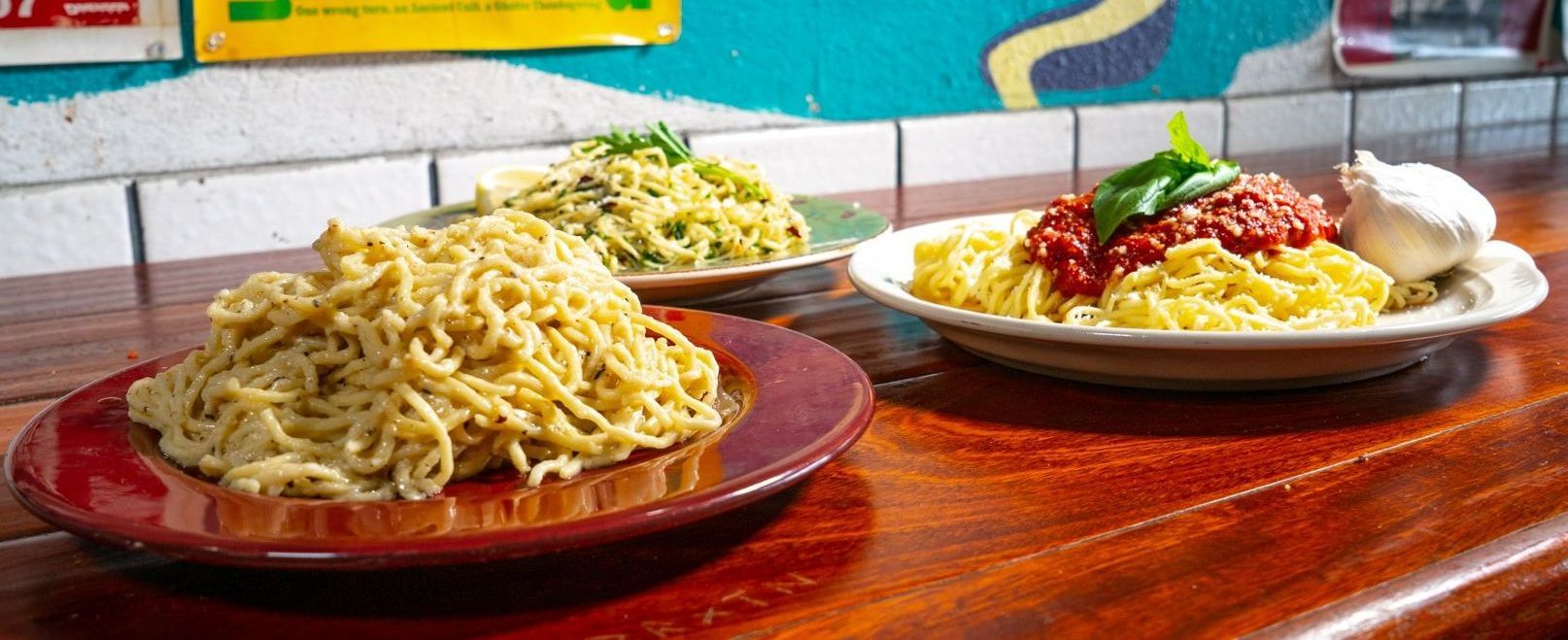 Three plates of spaghetti are on a wooden table