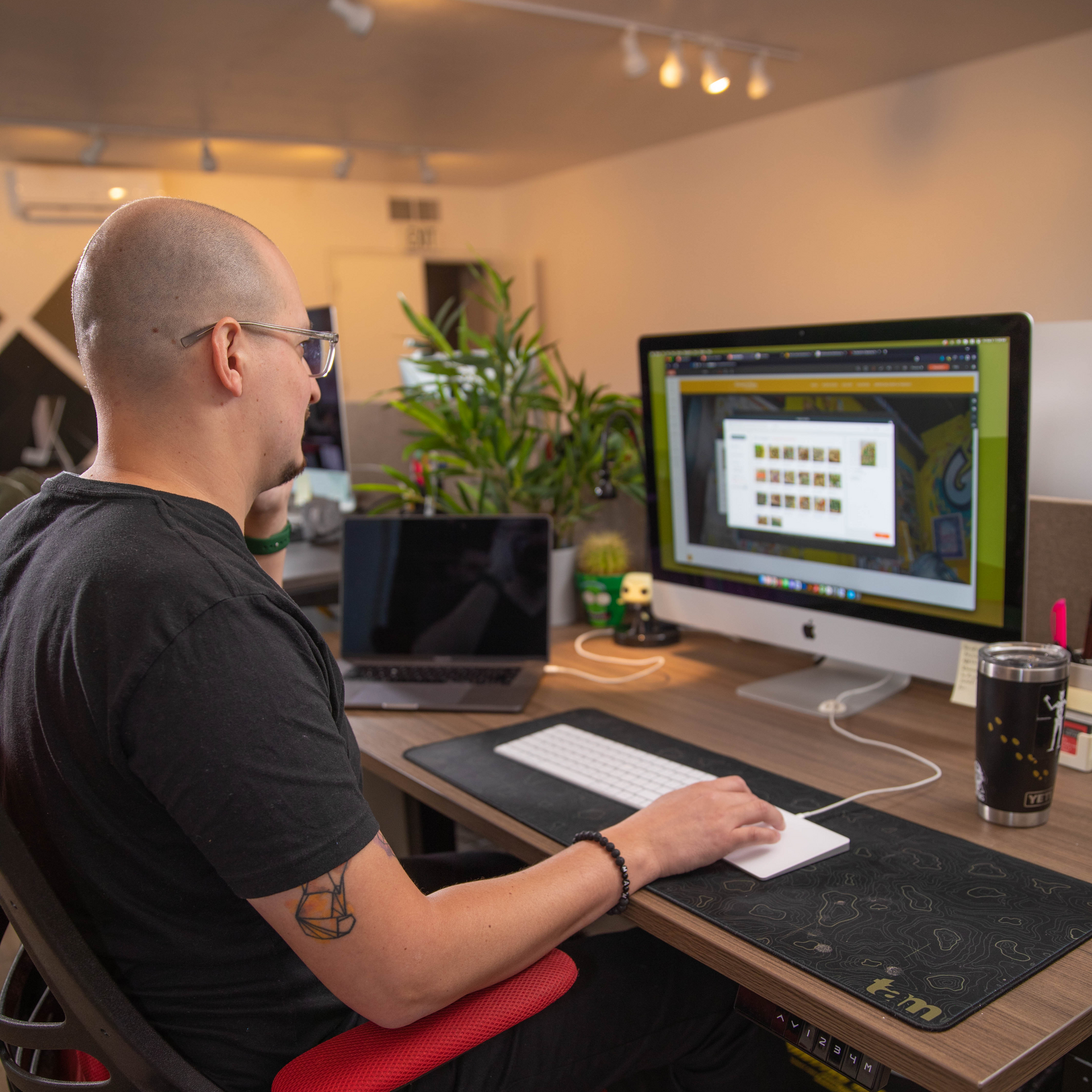 A man sits at a desk with a computer and a laptop