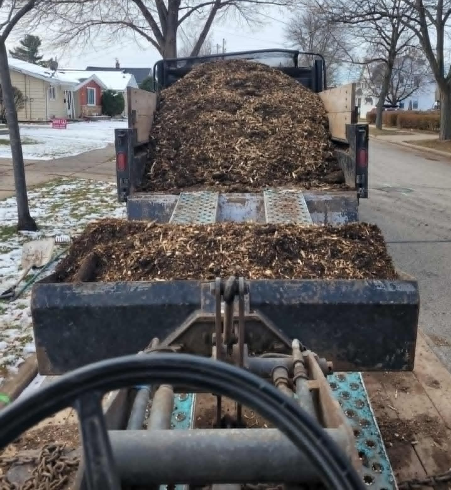 A yellow stump grinder cuts into a tree stump, throwing wood chips in an outdoor residential setting.