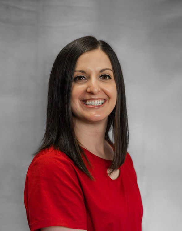 Woman with dark hair smiling, wearing a red top against a gray backdrop.