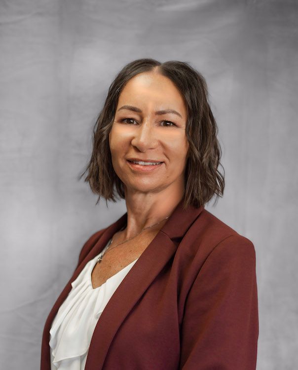 Woman in maroon blazer smiles, standing in front of a gray backdrop.