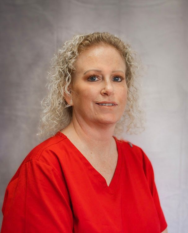 Woman with curly blonde hair wearing a red v-neck shirt, smiling against a white backdrop.