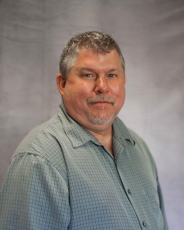 Man in a green button-down shirt smiles, posing against a gray gradient backdrop.