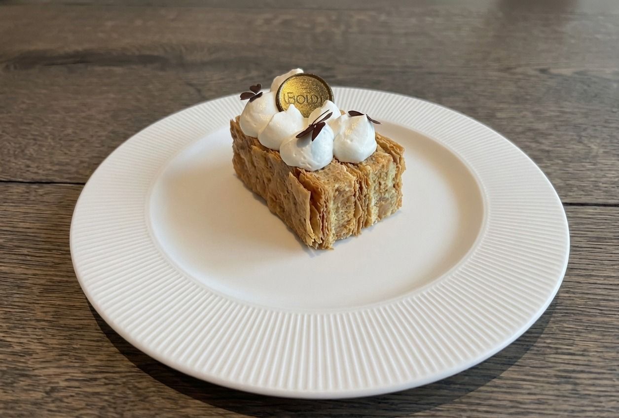 En lille, rektangulær mille-feuille-dej toppet med sprøjtet fløde og en dekorativ mønt på en hvid tallerken.