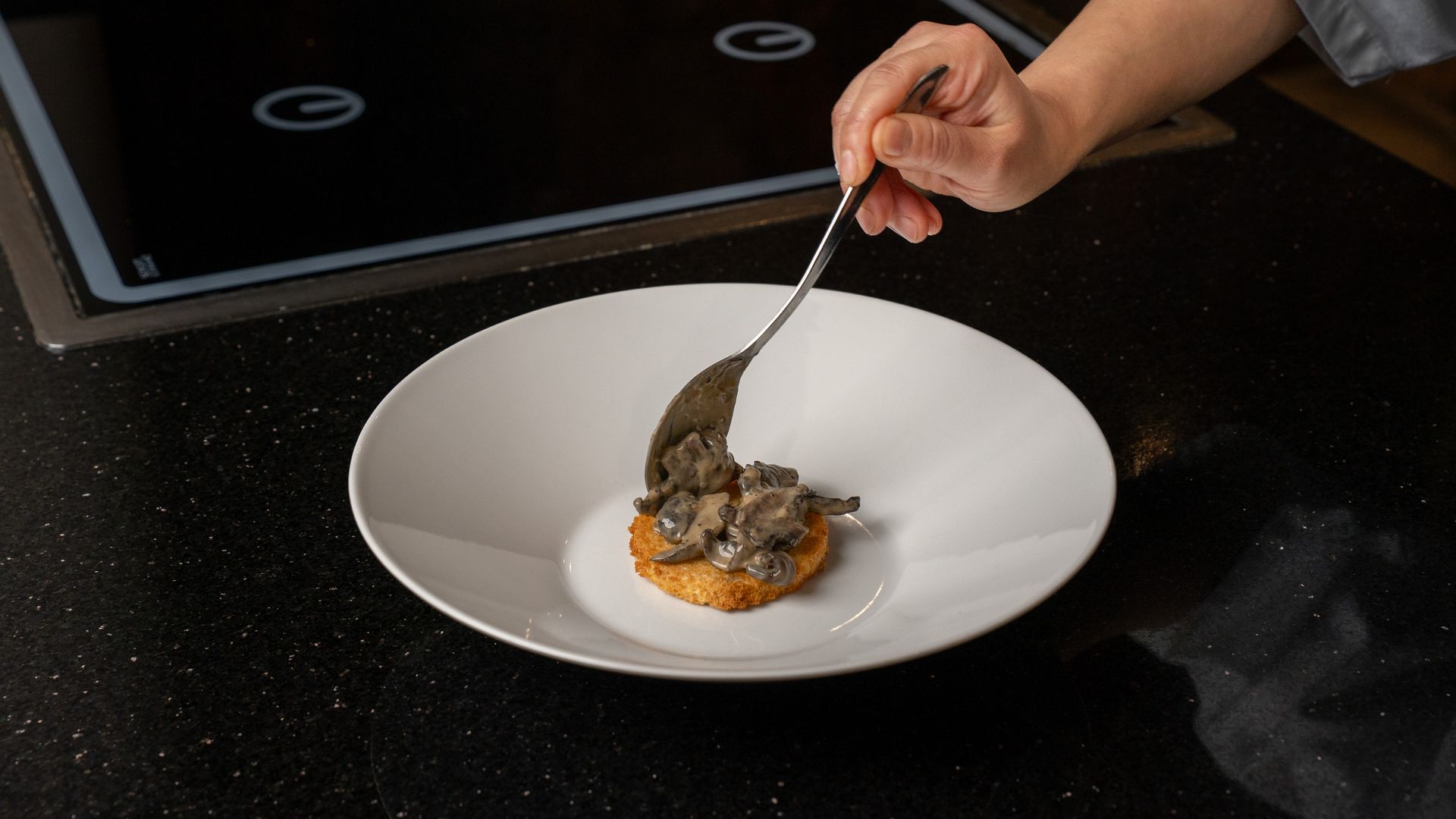 En håndanrettet mad på en hvid tallerken. En skefuld mørk topping placeres oven på en enkelt, ristet ret.