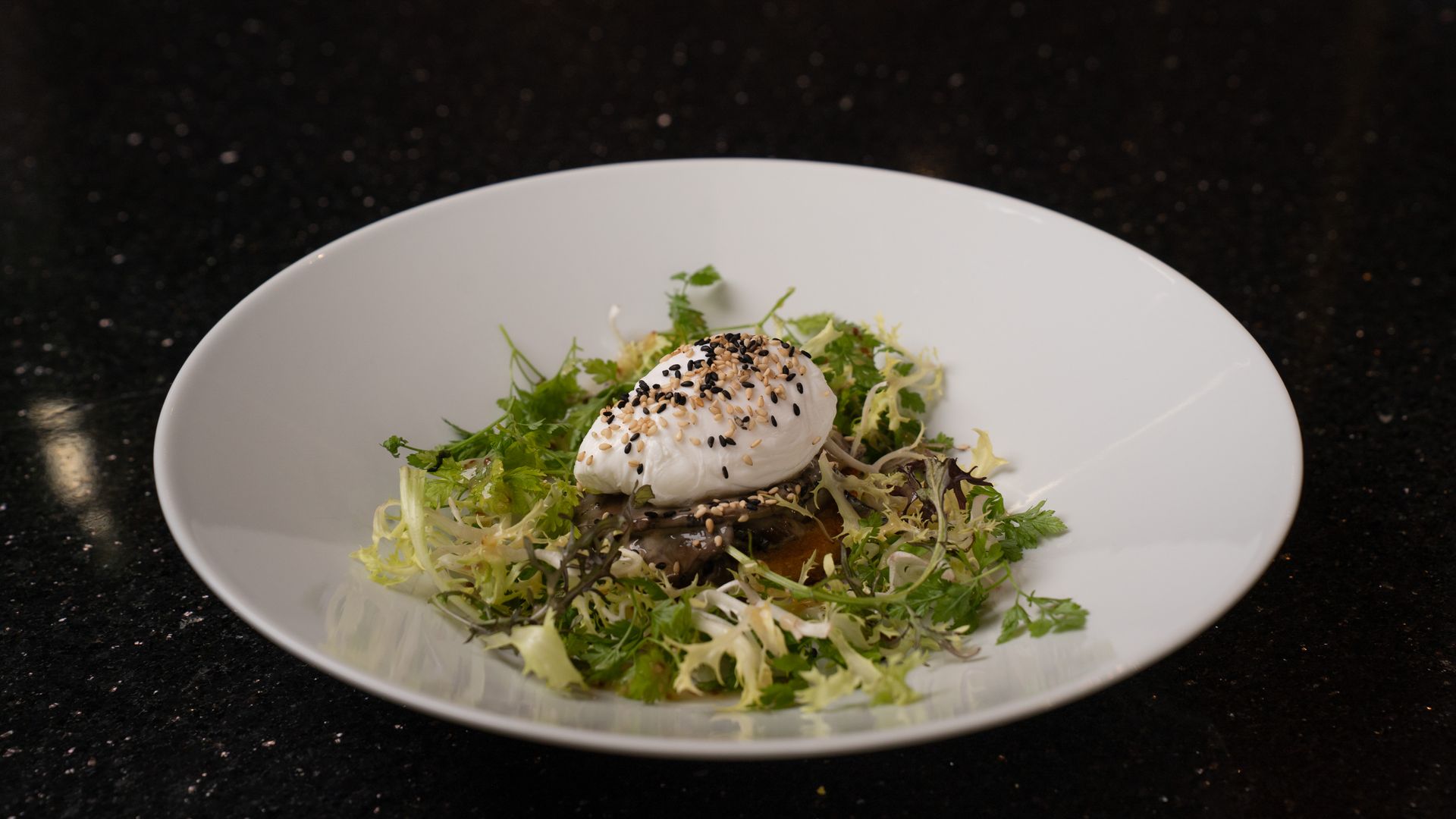 Salat med pocheret æg, spredte kerner på en hvid tallerken mod en mørk baggrund.