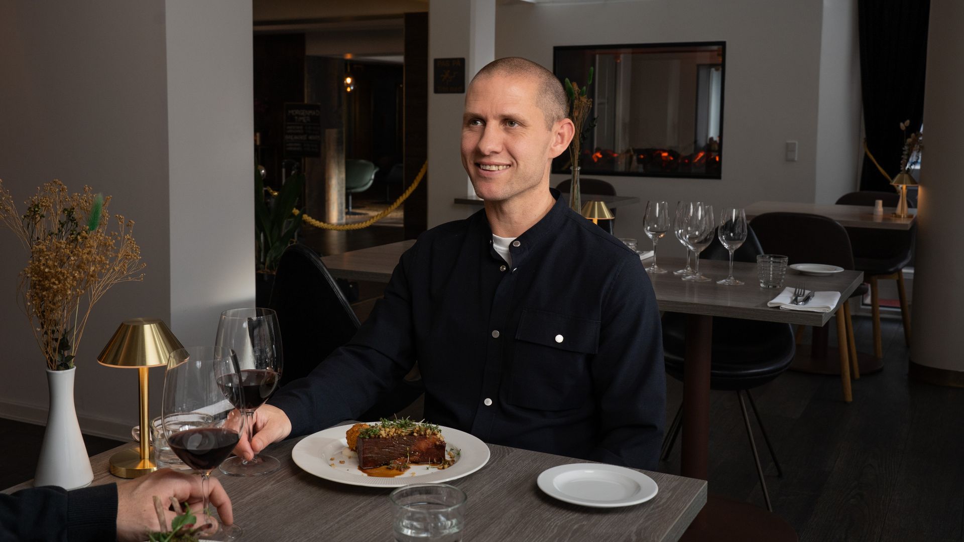 Mand siddende ved et restaurantbord med en tallerken mad og et glas vin.