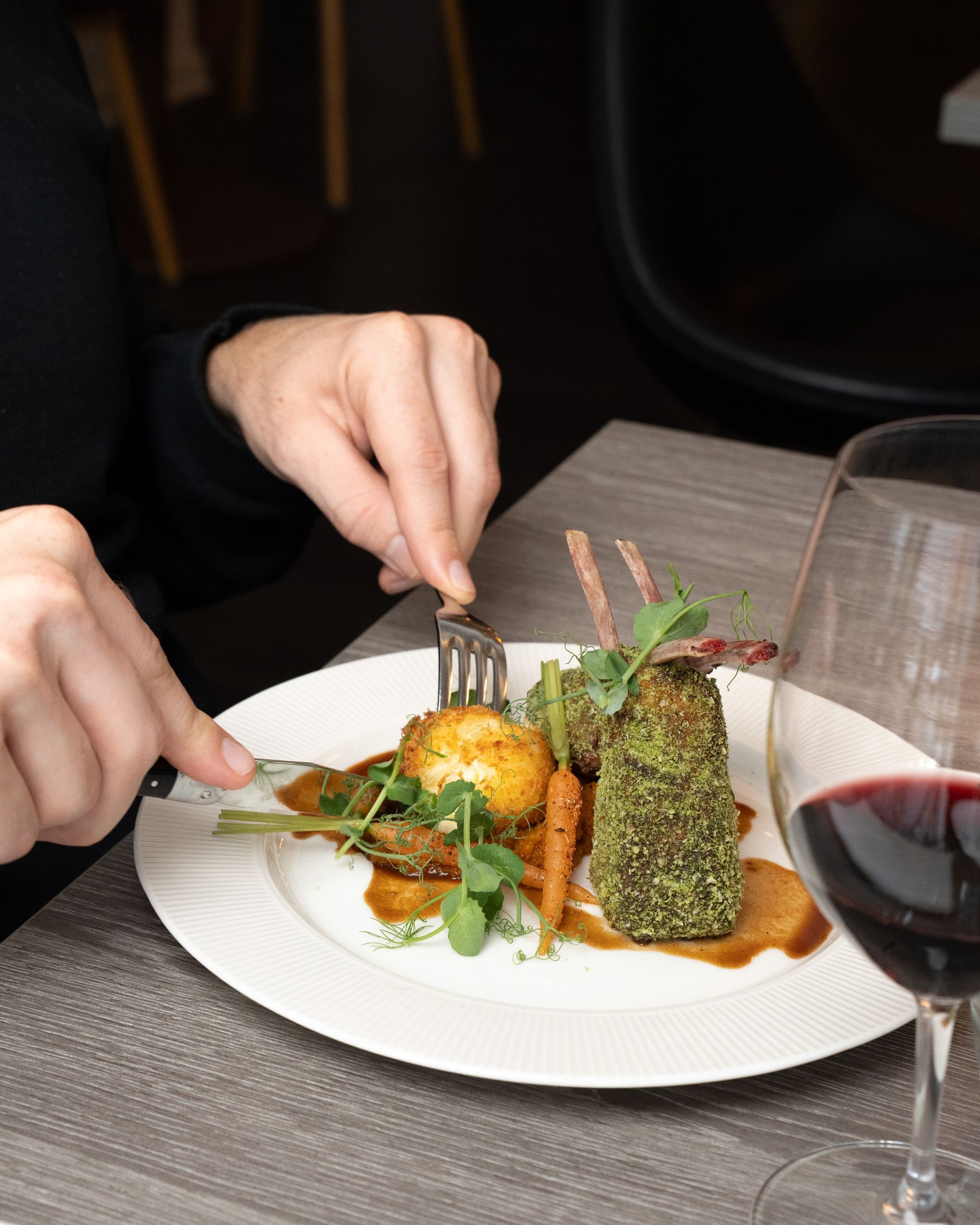 Person skærer i et gourmetmåltid på en hvid tallerken med rødvin i glasset.