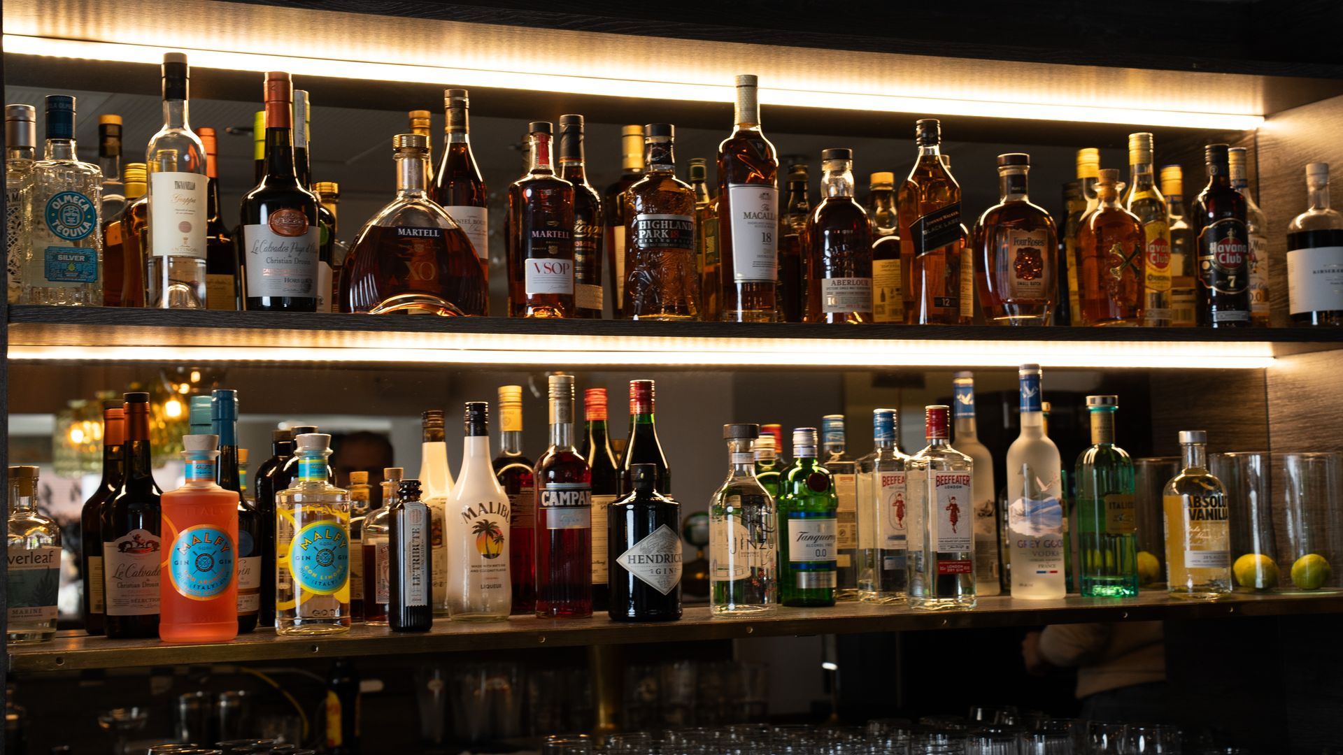 Hylder med spiritusflasker bag en bar. Brune, klare og farverige flasker er oplyst.