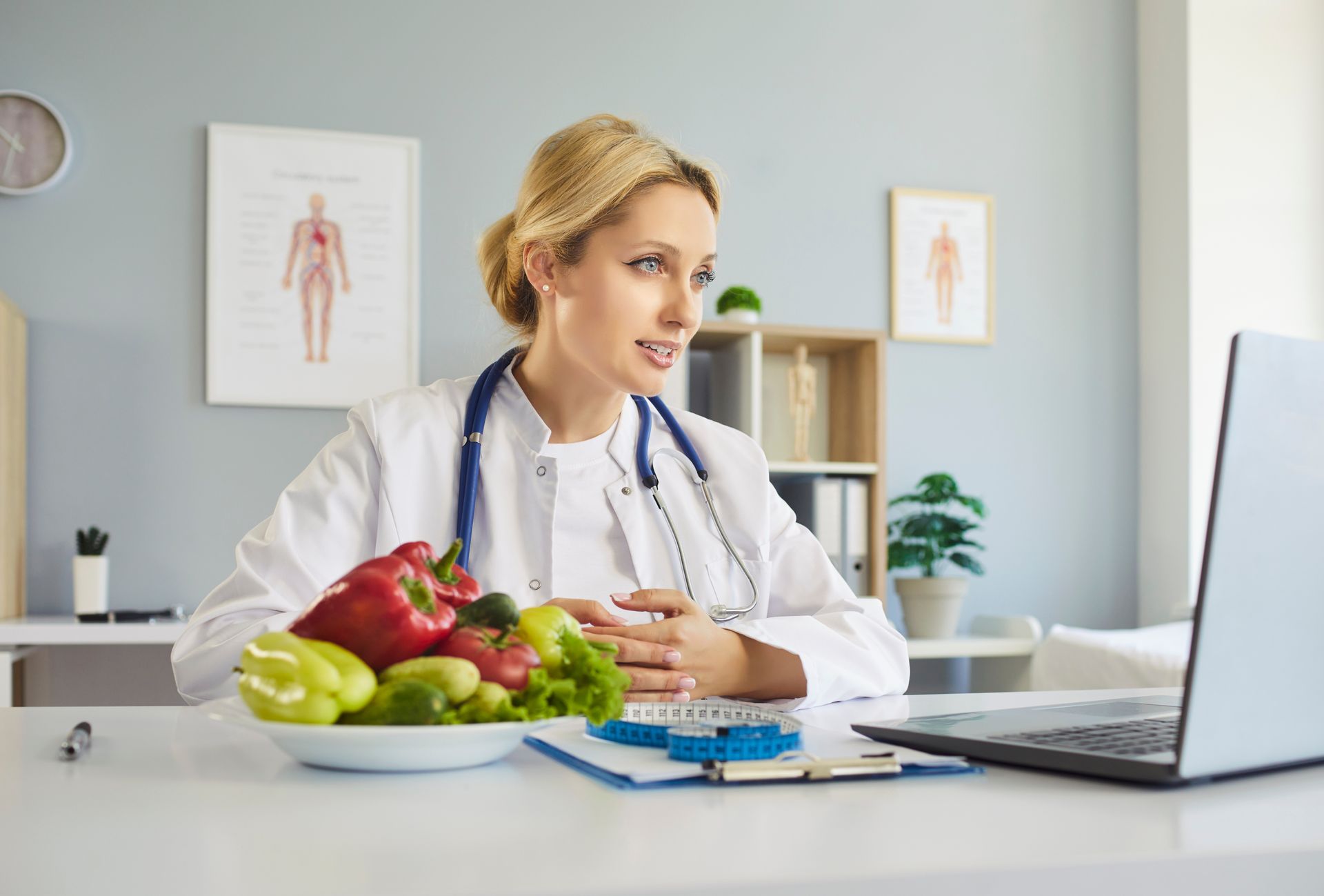 Nutritionist in white coat consulting at a desk with fruit, a notebook, and a laptop in a bright office