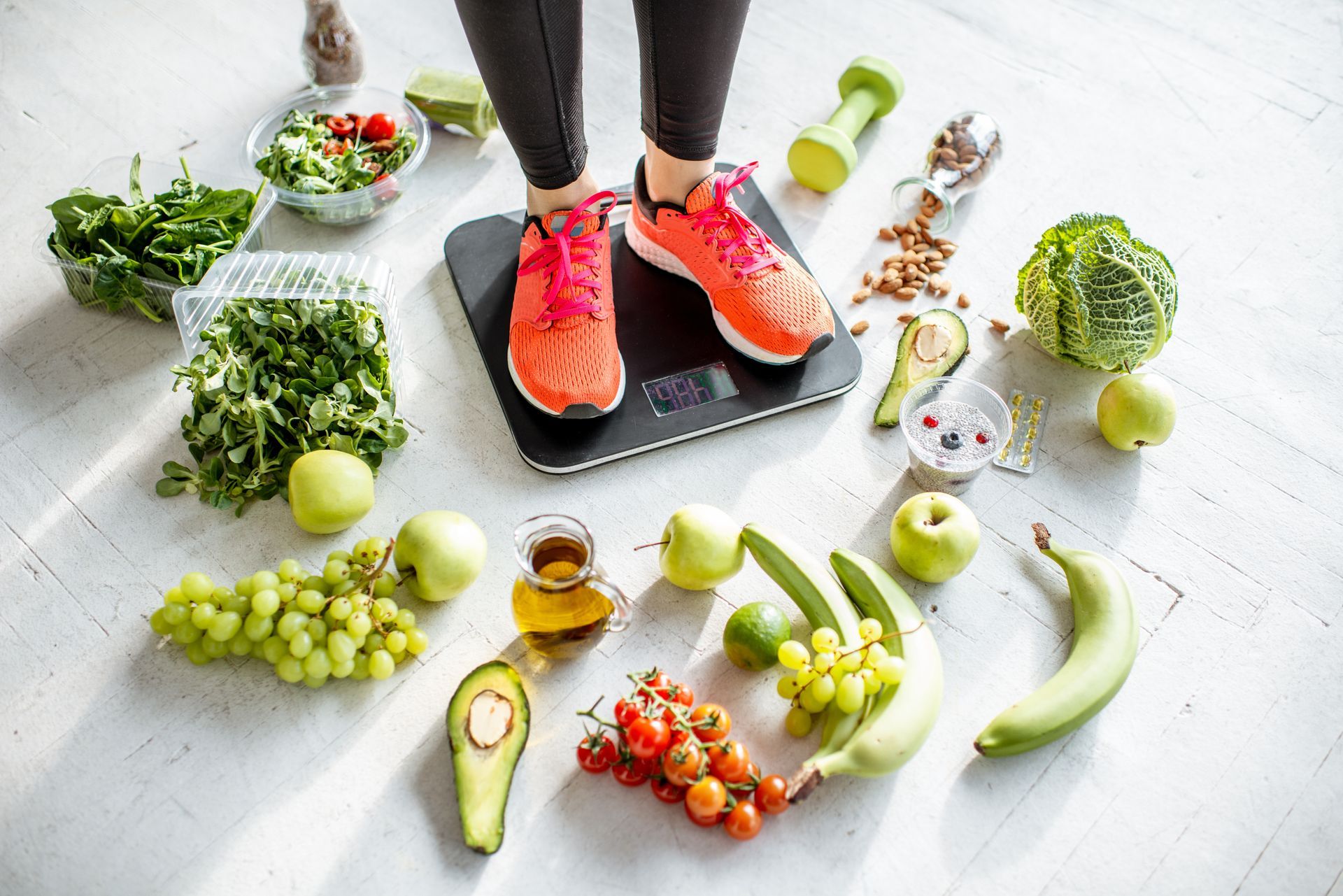 Person standing on a scale surrounded by fruits and vegetables on a white floor