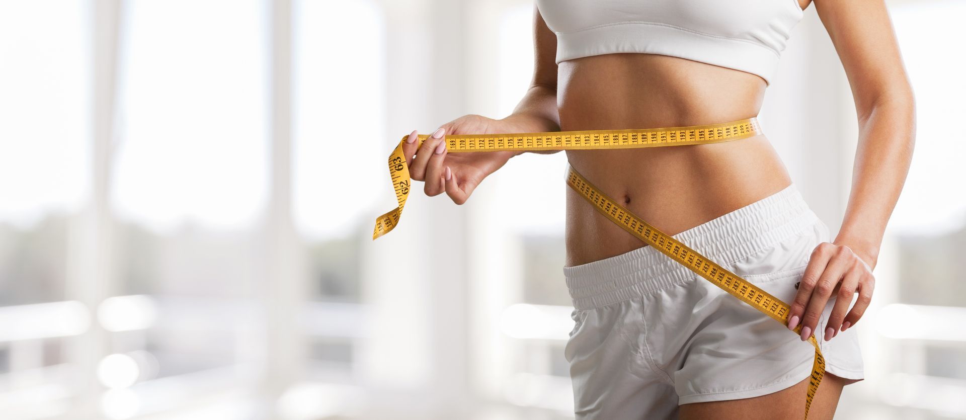 Person measuring waist with a yellow tape measure in a bright indoor setting