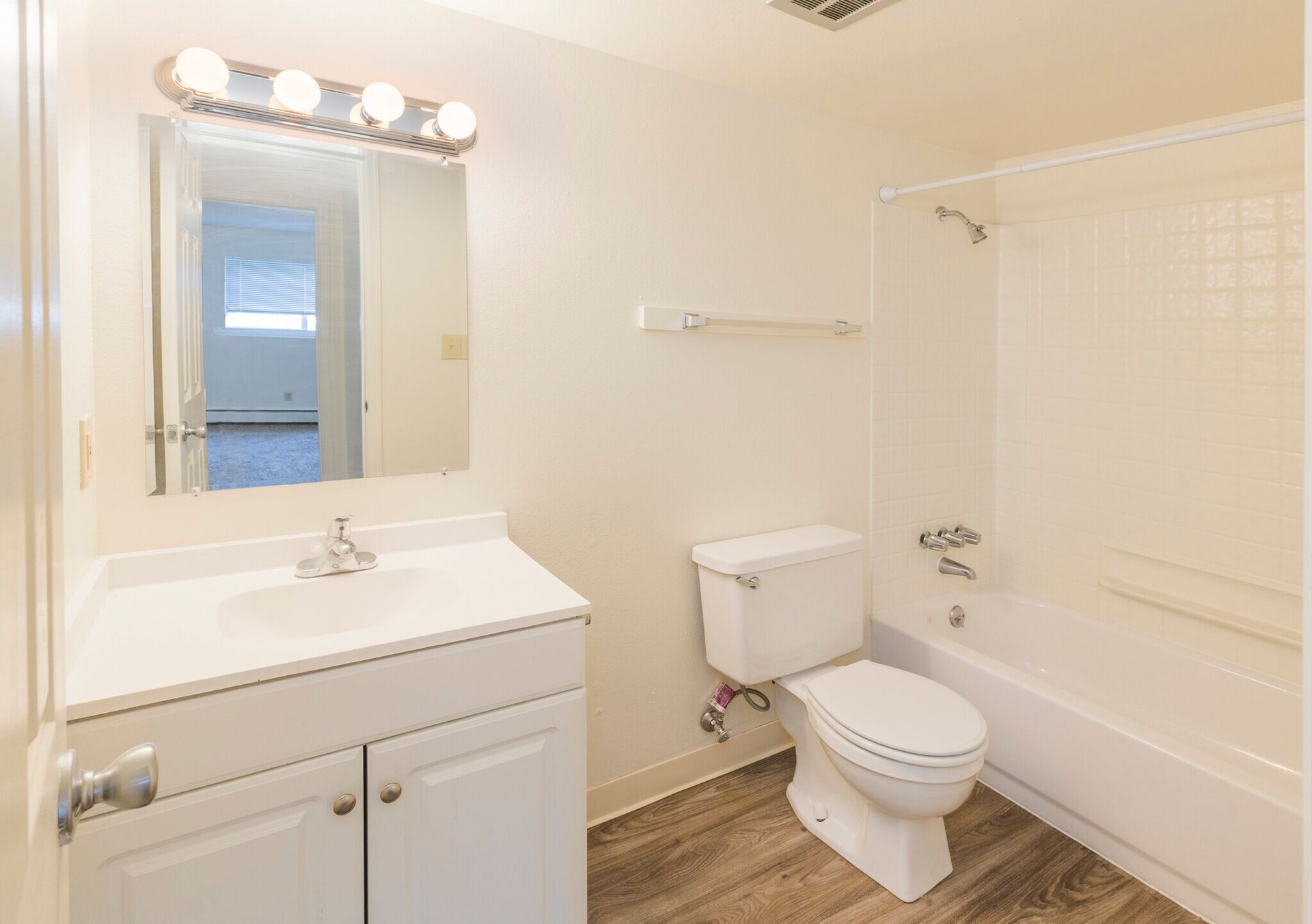 Bathroom with a white vanity, toilet, and bathtub. Light wood-look flooring. Mirror with overhead lighting.