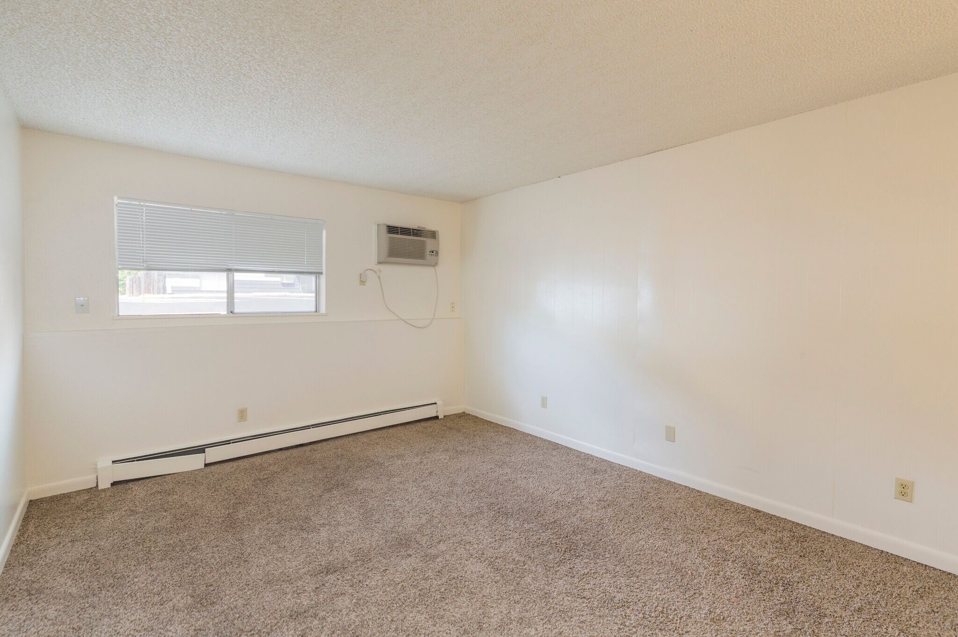 Empty bedroom with beige carpet, white walls, and a window with blinds.