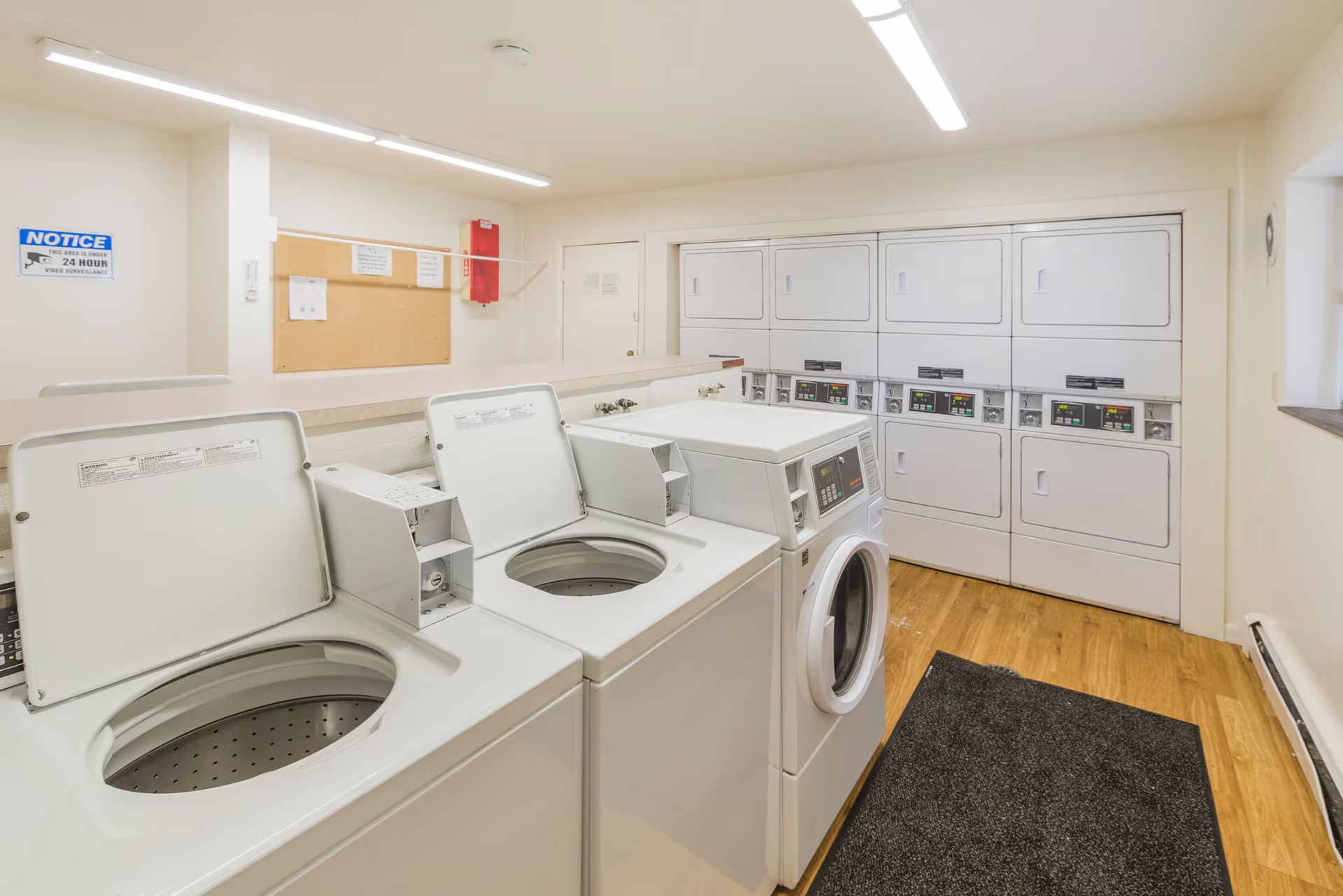 Laundry room with multiple white washing machines, dryers, and a bulletin board.