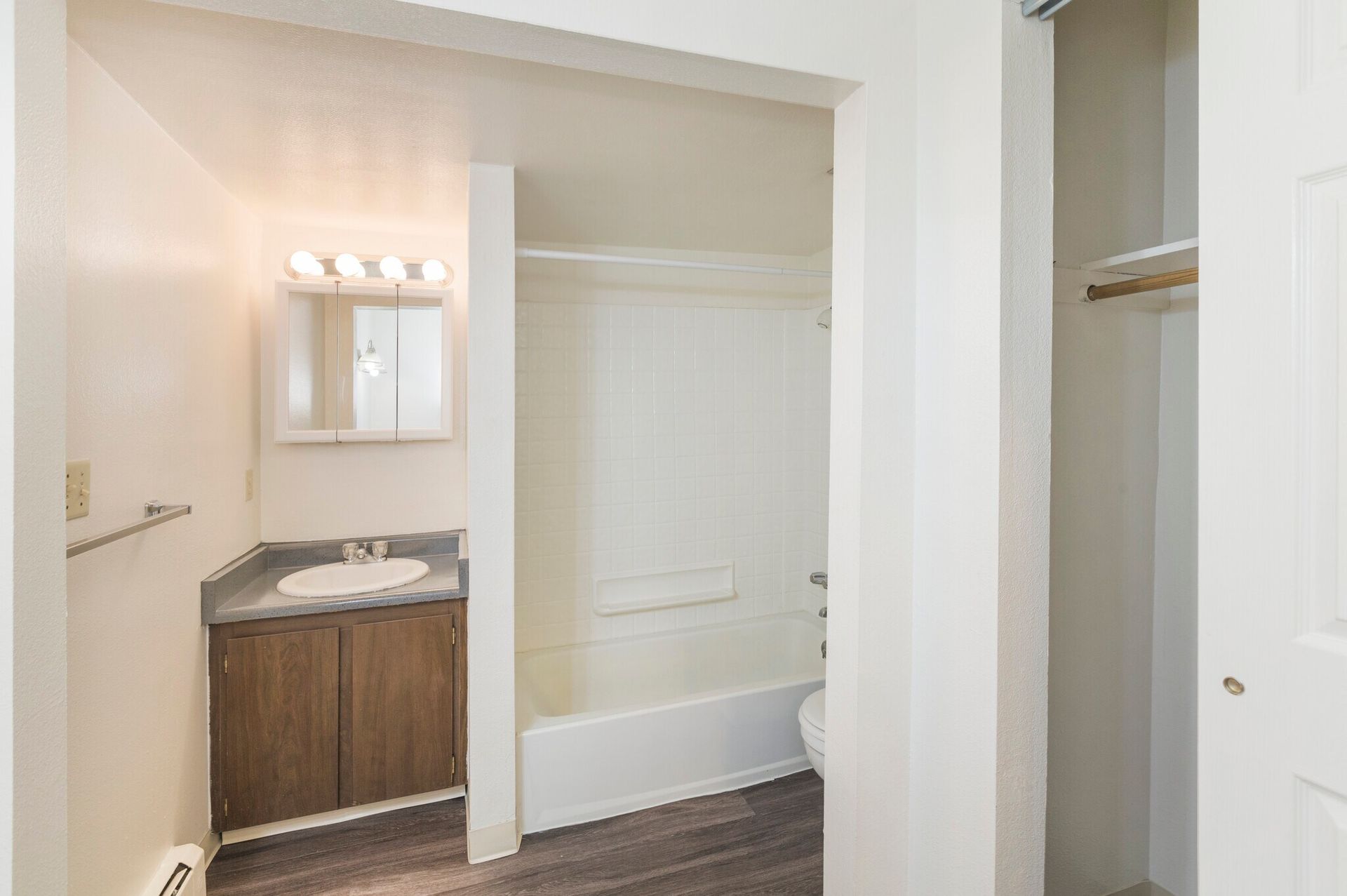 Bathroom with white walls, tub, vanity, and a closet with a hanging rod.