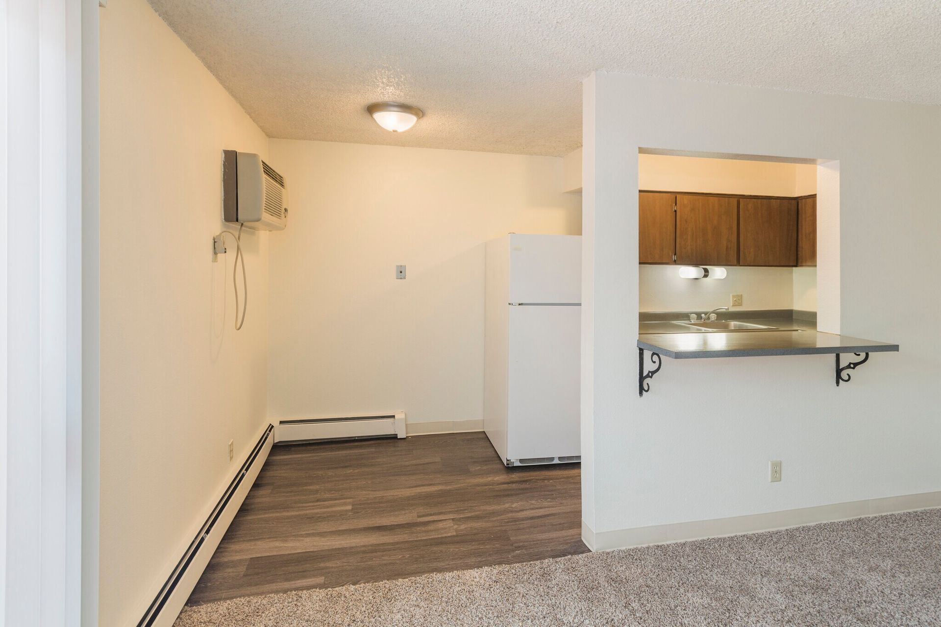 Interior view of an apartment with a kitchen pass-through, refrigerator, and wood-look flooring.