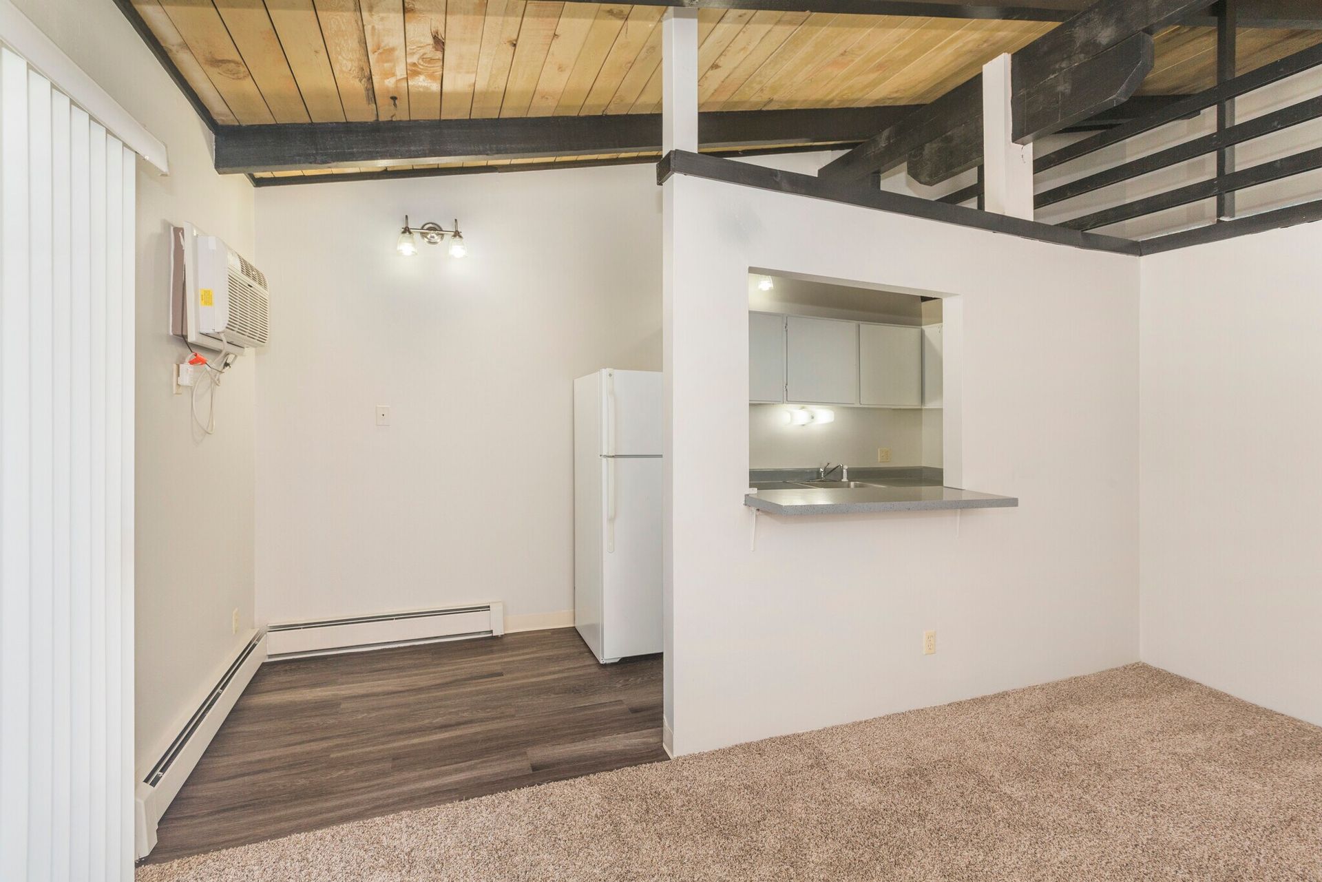 Interior of a small apartment with a kitchen area, white walls, and wood-beam ceiling.