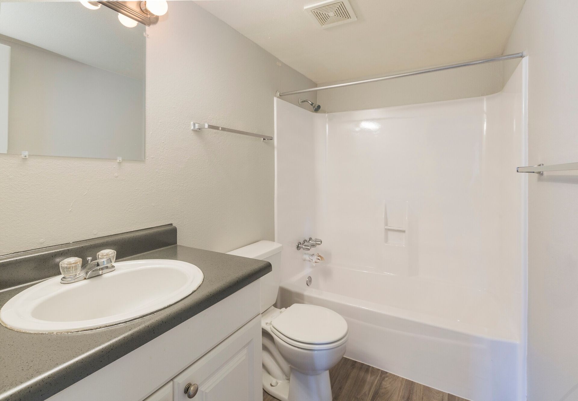Bathroom with a white bathtub and toilet, sink with gray countertop, and a mirror on the wall.