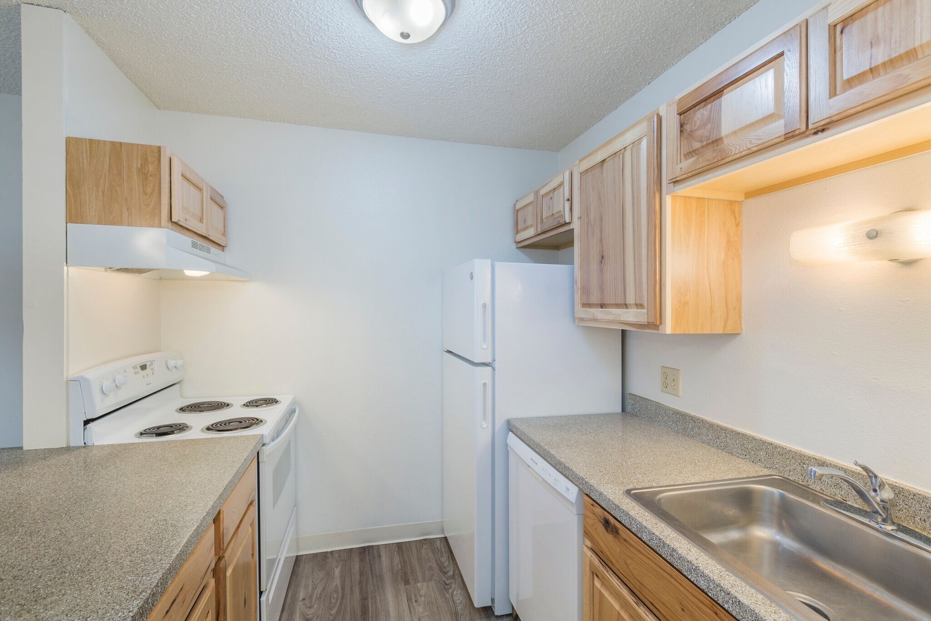 Small kitchen with light wood cabinets, white appliances, and gray countertops.