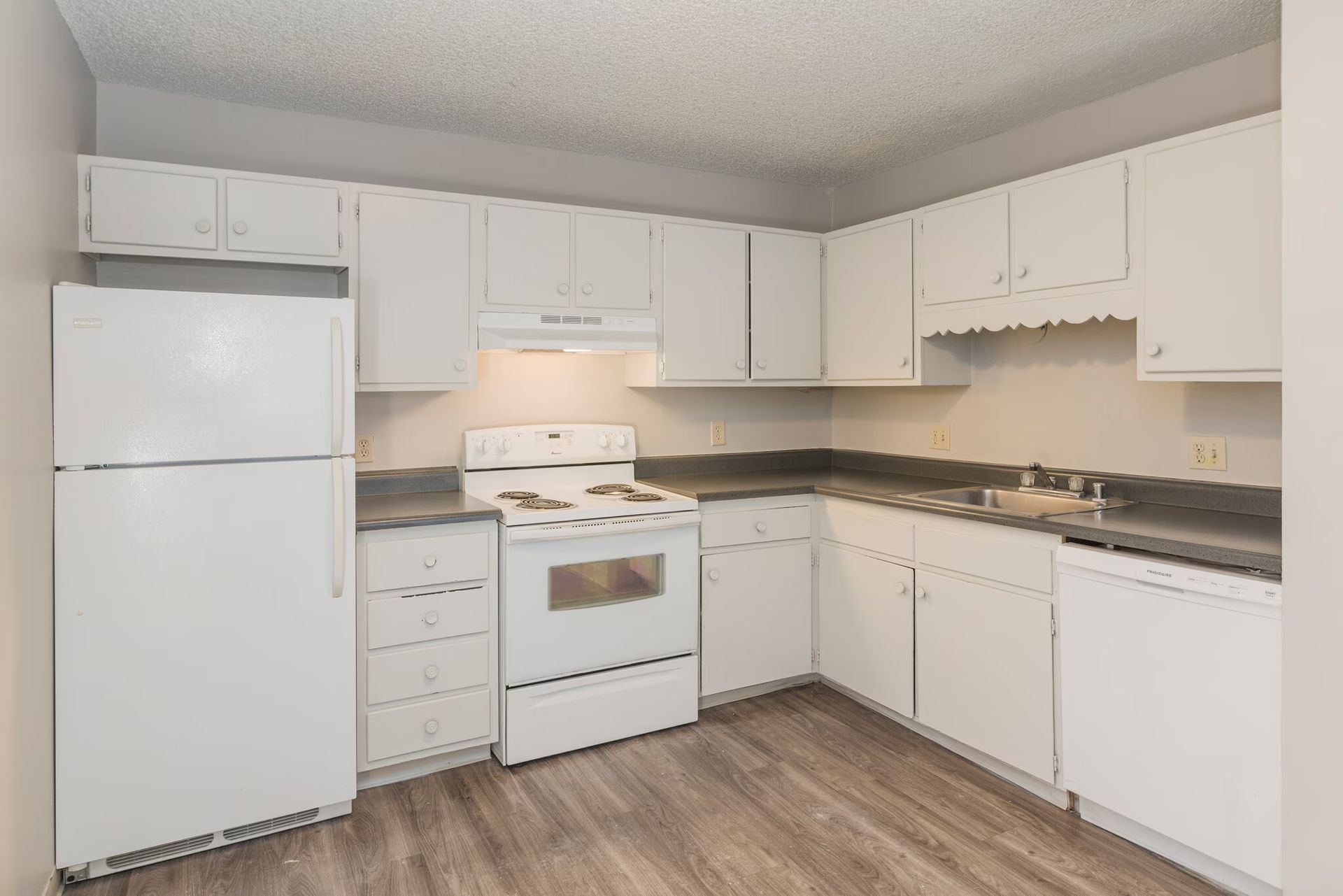 White kitchen with appliances, cabinets, countertops, and wood-look flooring.