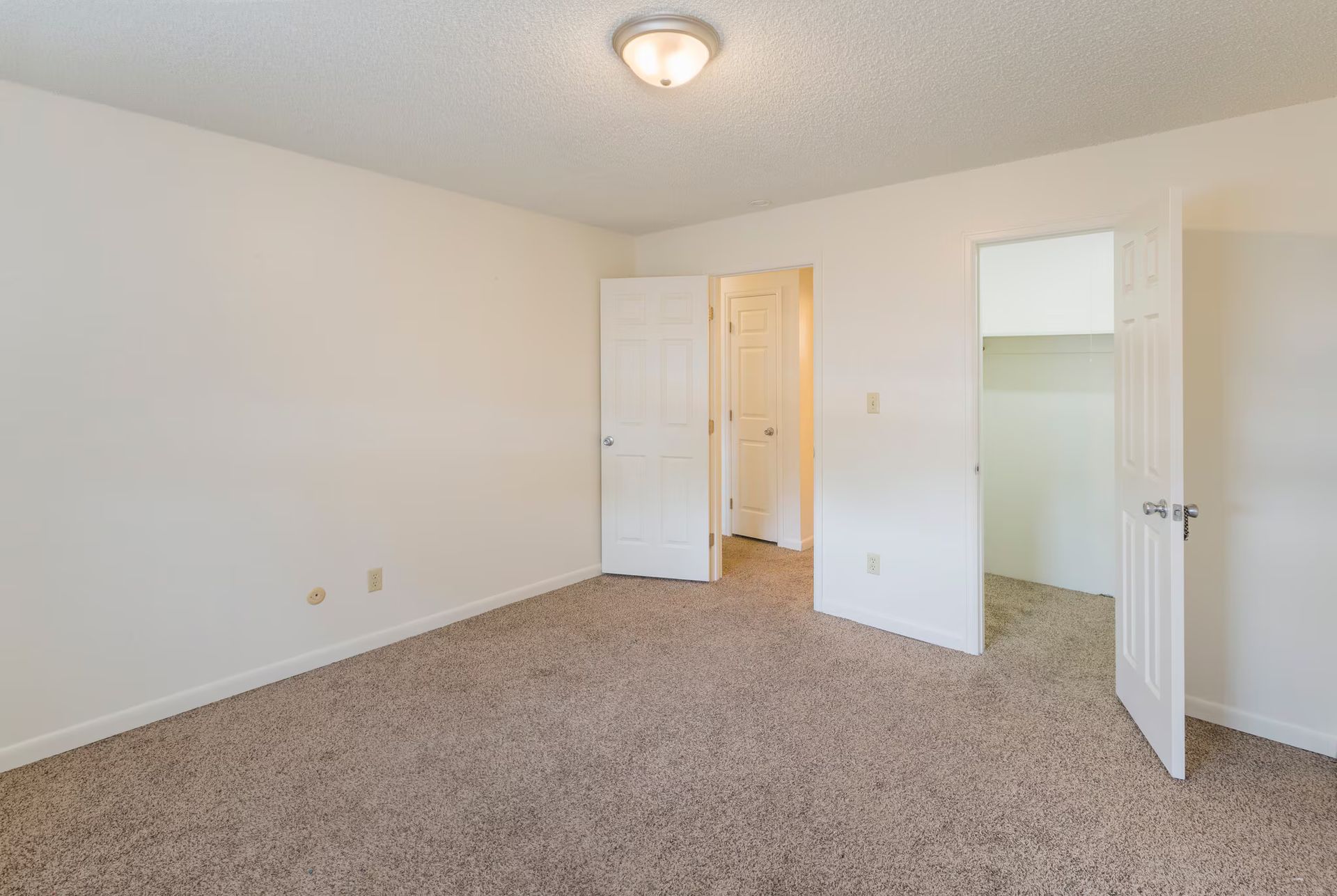 Empty room with beige carpet, white walls, two closed doors, and a closet.