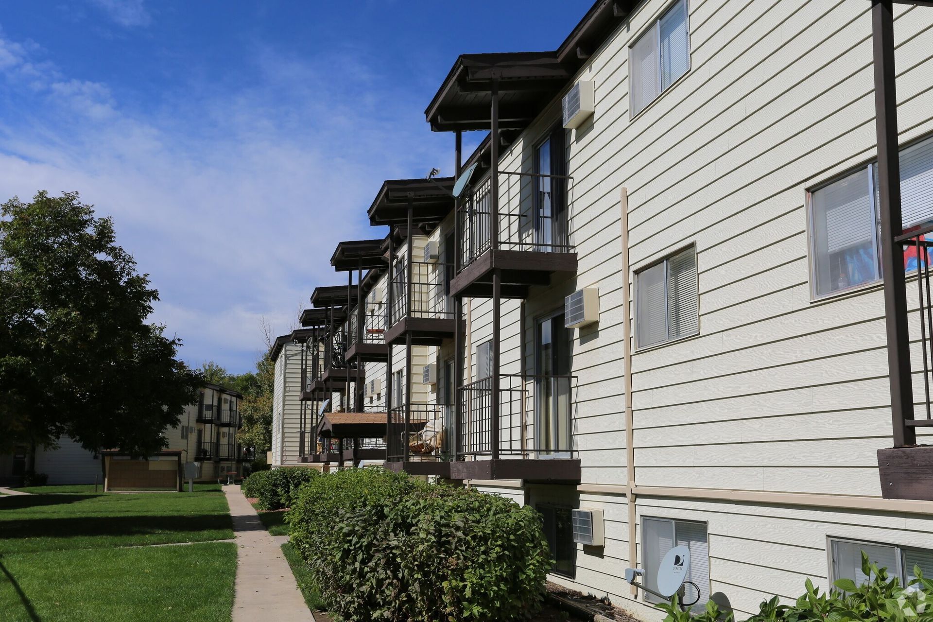Apartment building with balconies and a small patch of grass under a blue sky.