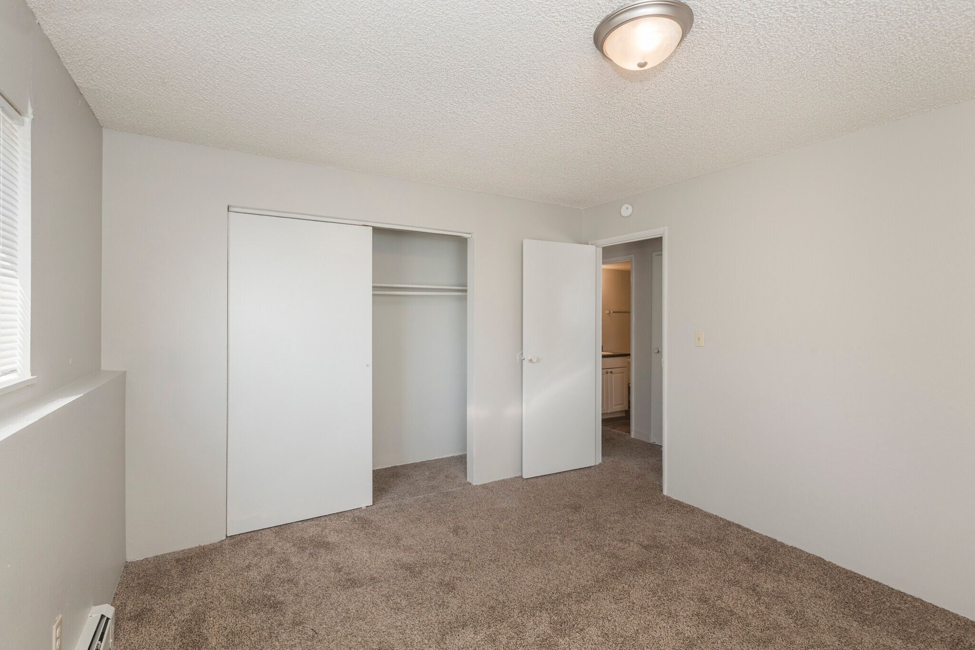 Empty bedroom with sliding closet doors, brown carpet, and a door leading to a bathroom.
