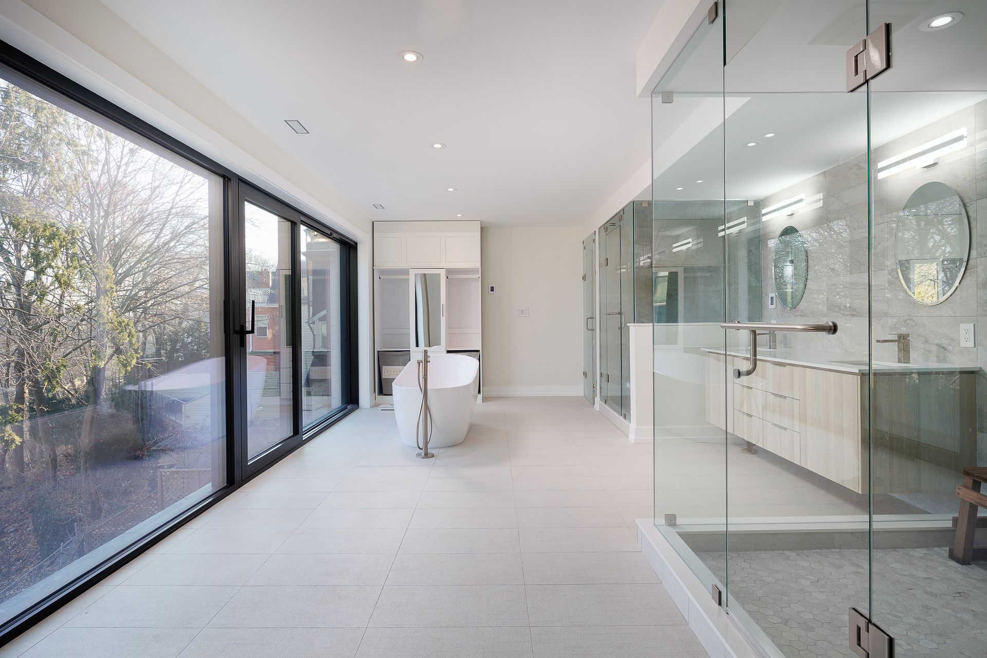Bright modern bathroom with glass shower, double vanity, and large floor-to-ceiling windows