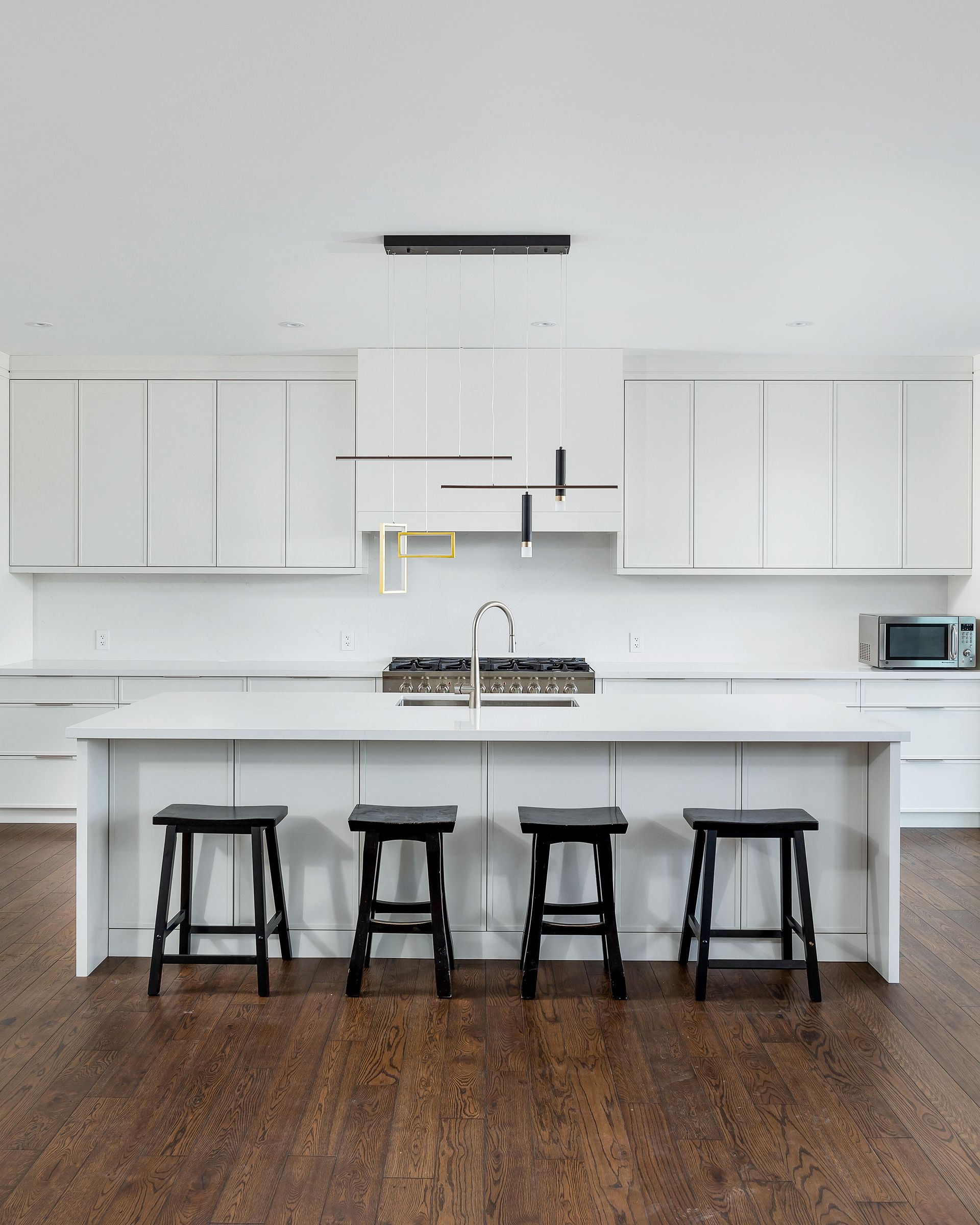 Modern white kitchen with a large island, four black stools, and hardwood floors
