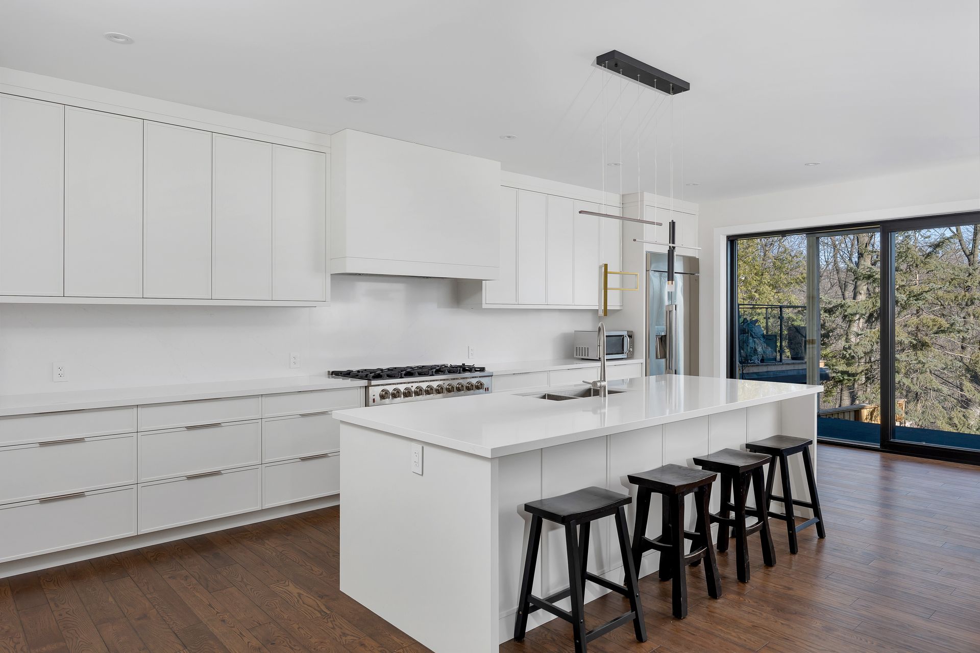 Bright modern white kitchen with island, black stools, and large sliding glass doors