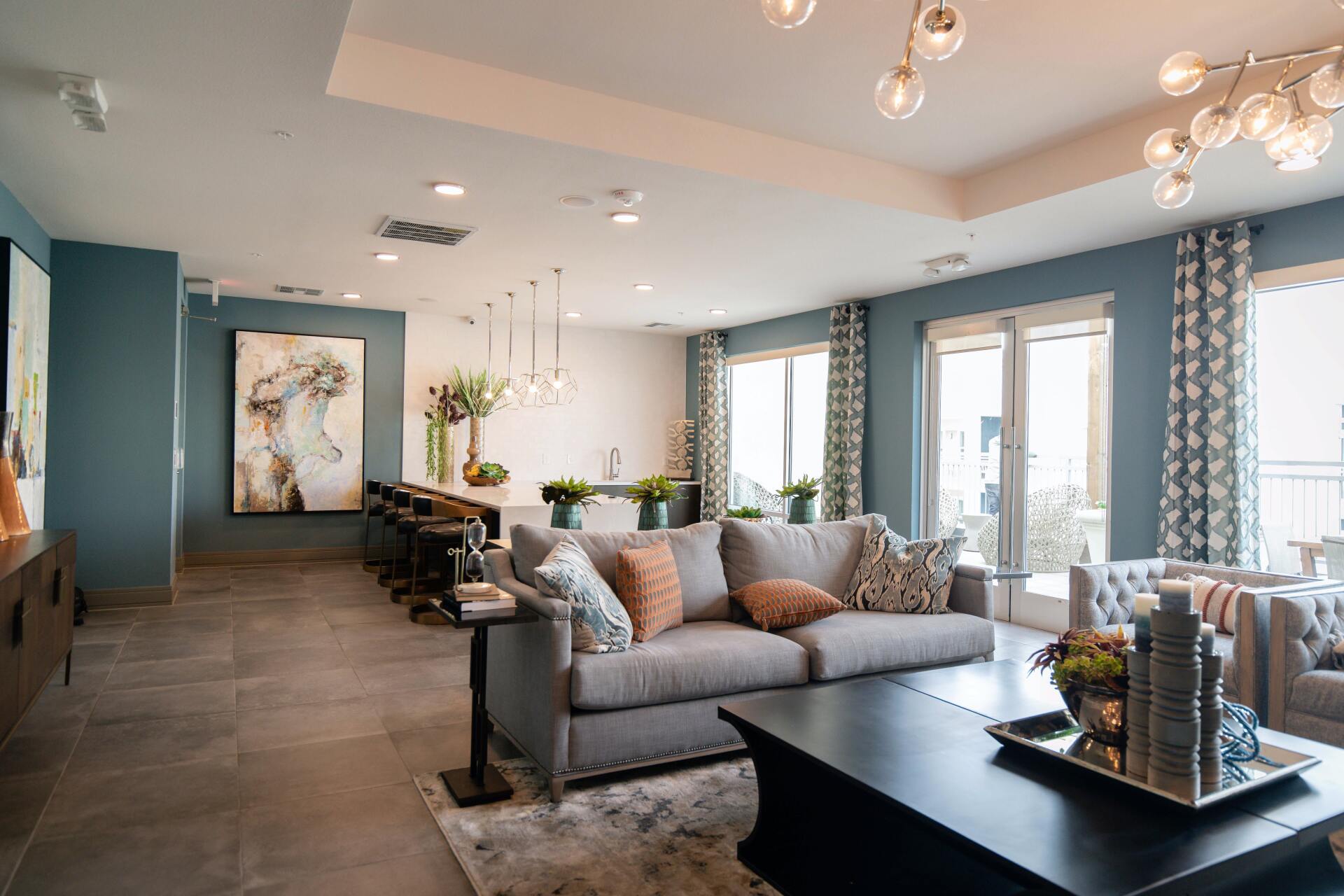 Spacious modern living room with gray sectional sofa, coffee table, and large windows with patterned curtains