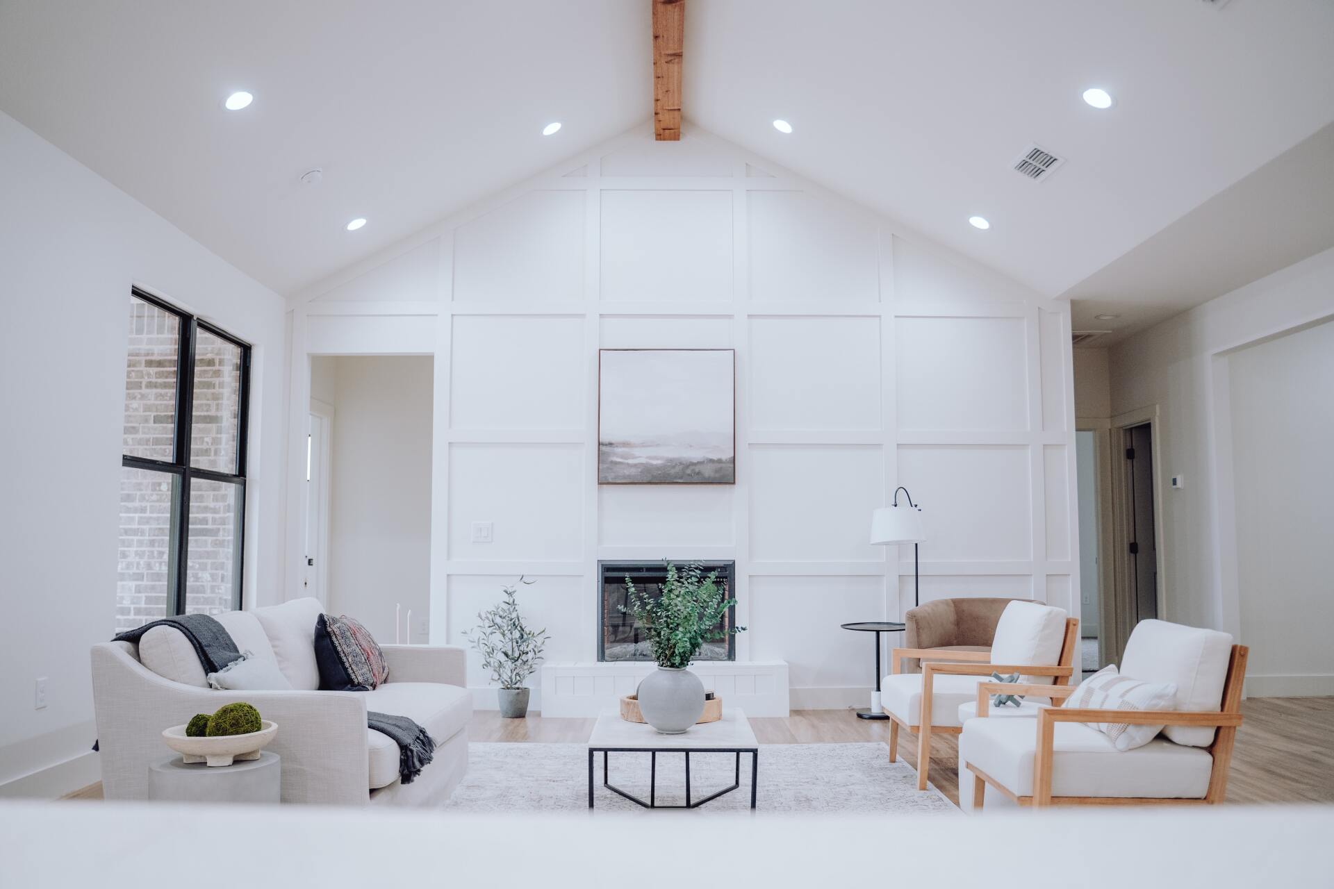 Bright white modern living room with vaulted ceiling, fireplace, and two chairs by windows.