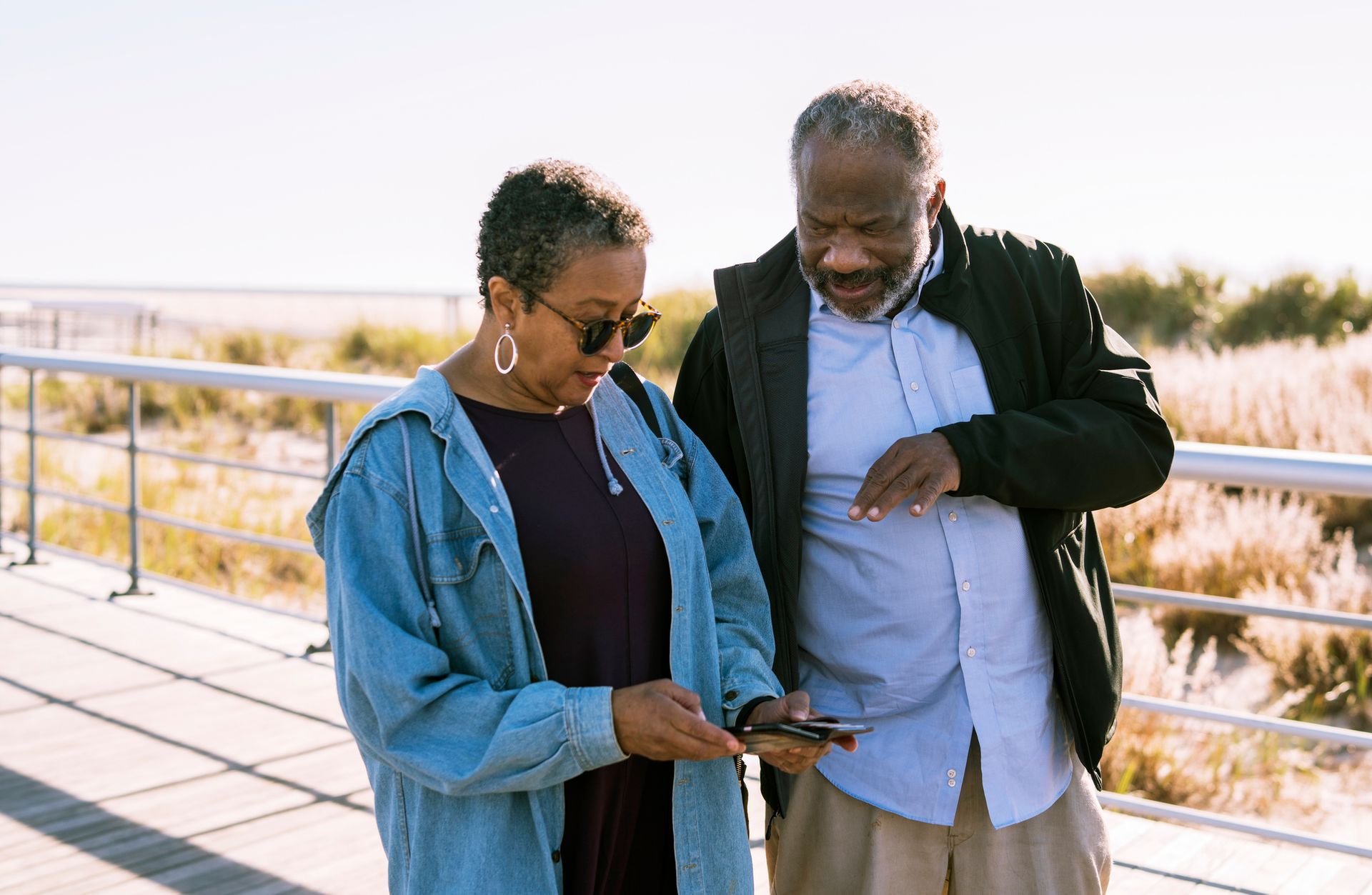 African American black couple looking at a phone on a boardwalk near a beach; sunny day.
